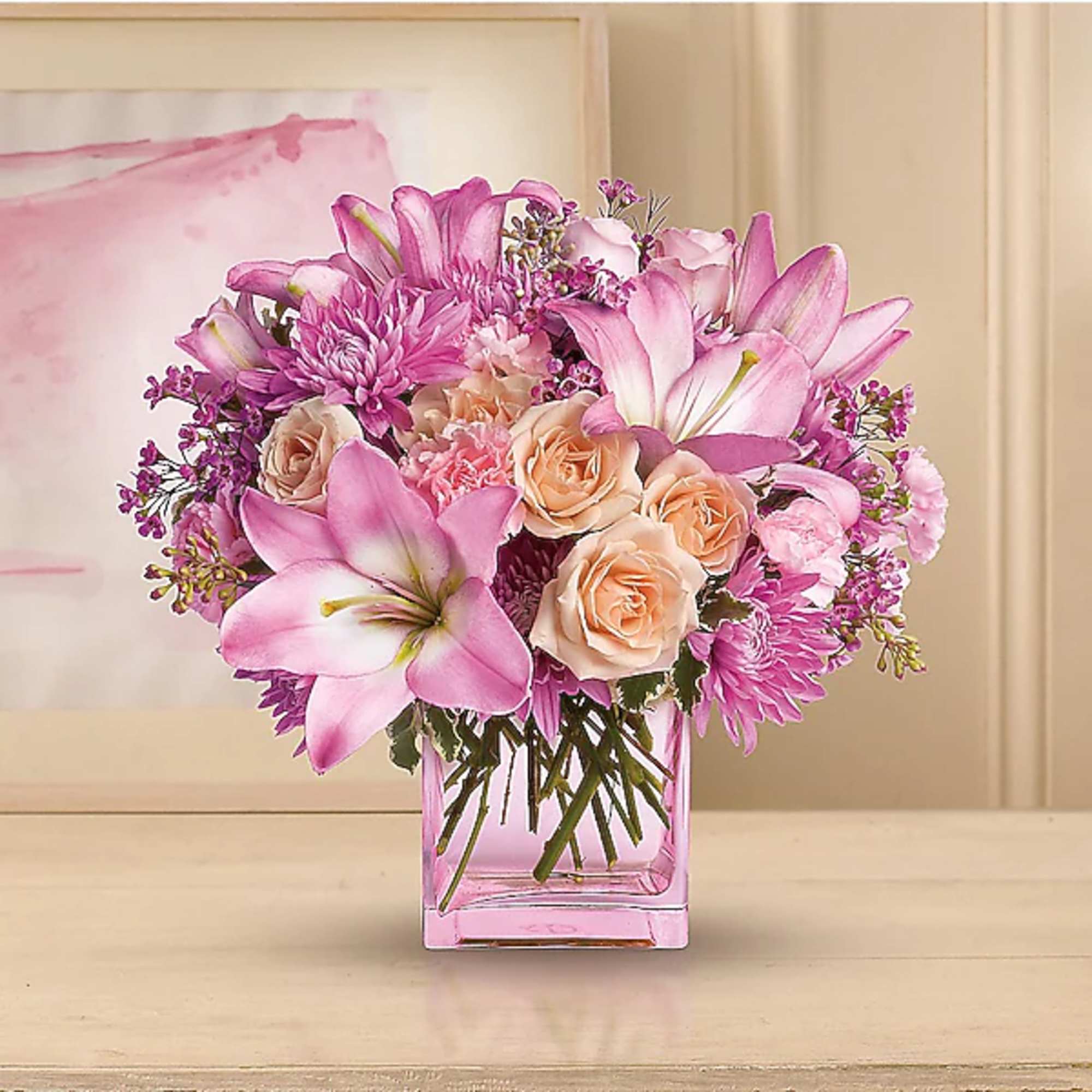 Pink lilies and peach roses arranged in a square glass vase