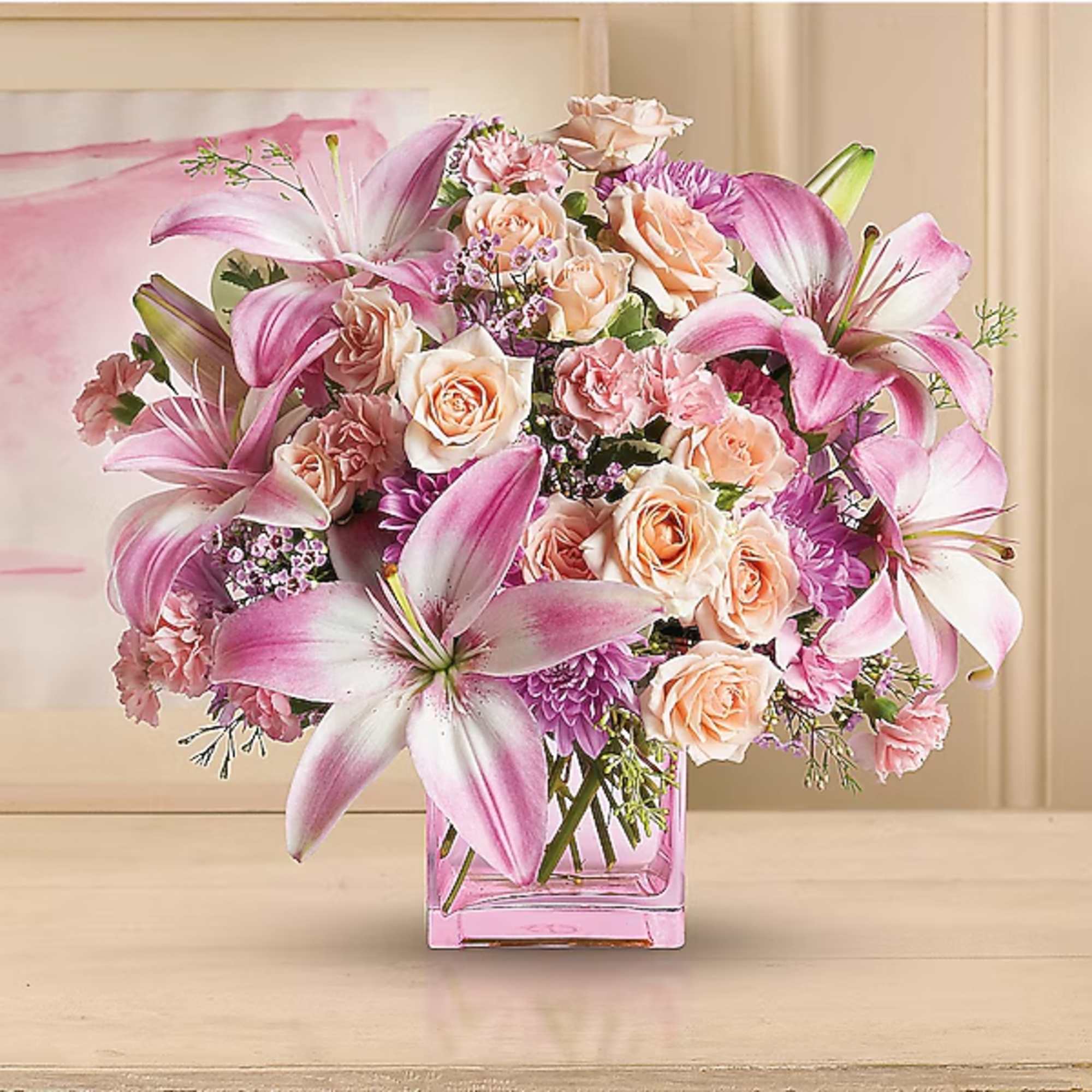 Pink lilies and peach roses arranged in a square glass vase