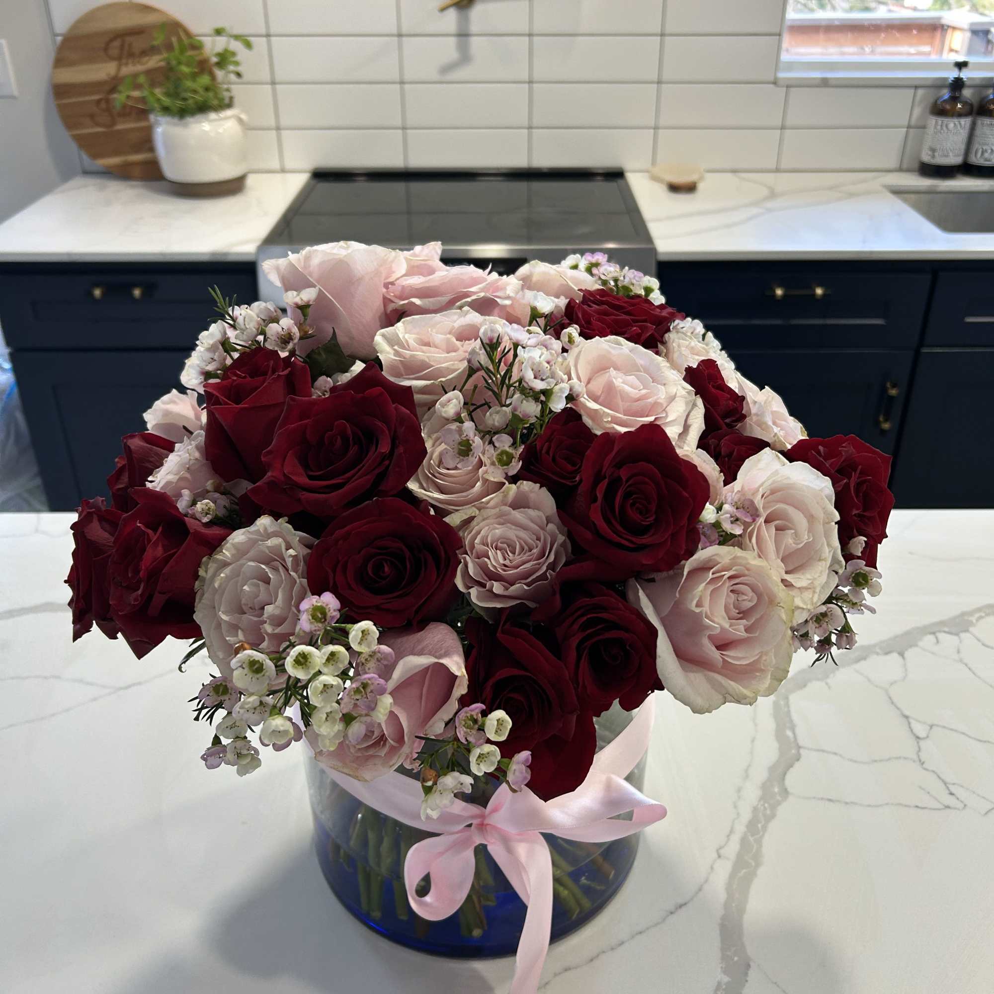 Bouquet of red and blush roses in a blue vase with a pink ribbon