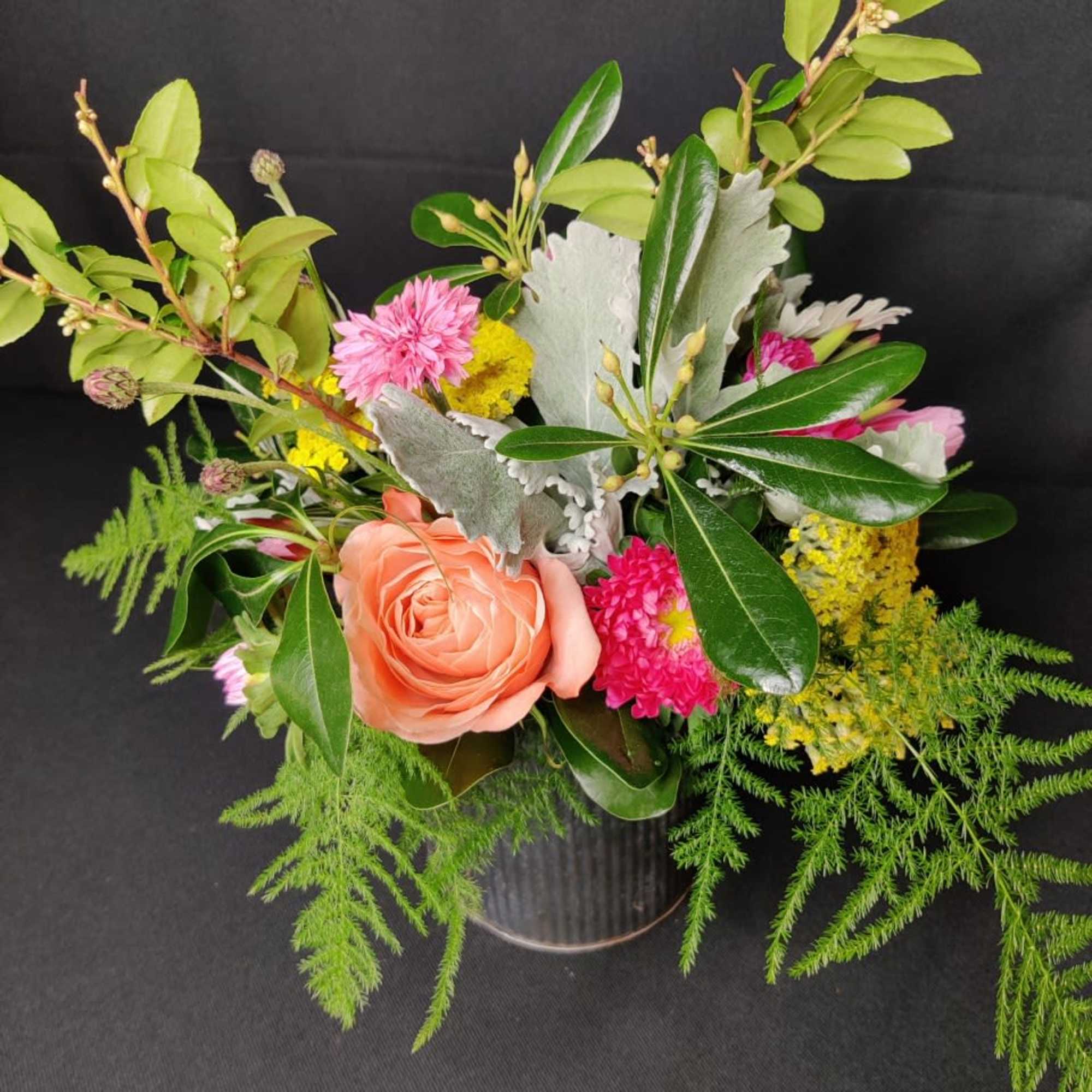 Mixed bouquet with a peach rose, pink blooms, and greenery in a vase