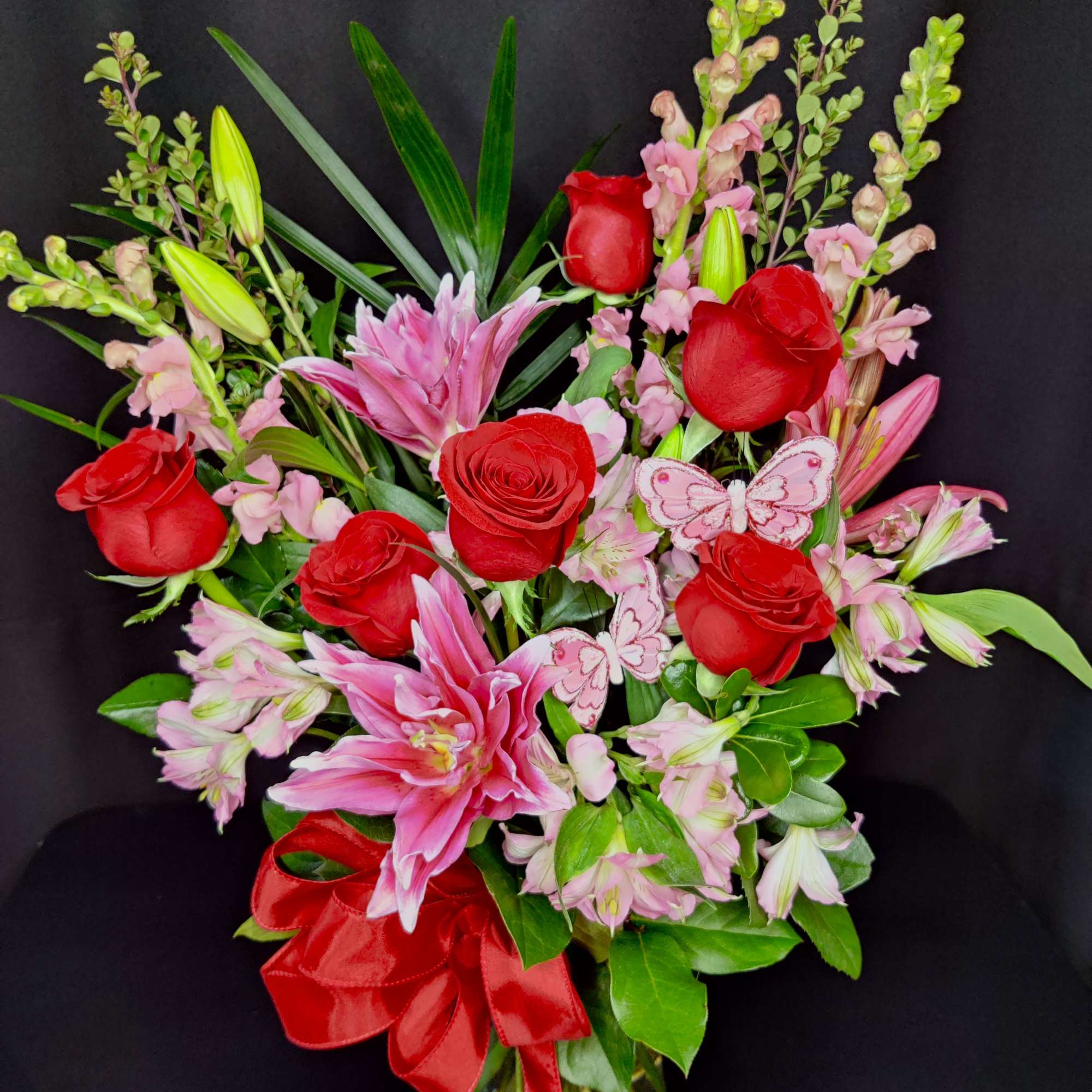 Red roses and pink lilies in a glass vase with a red ribbon