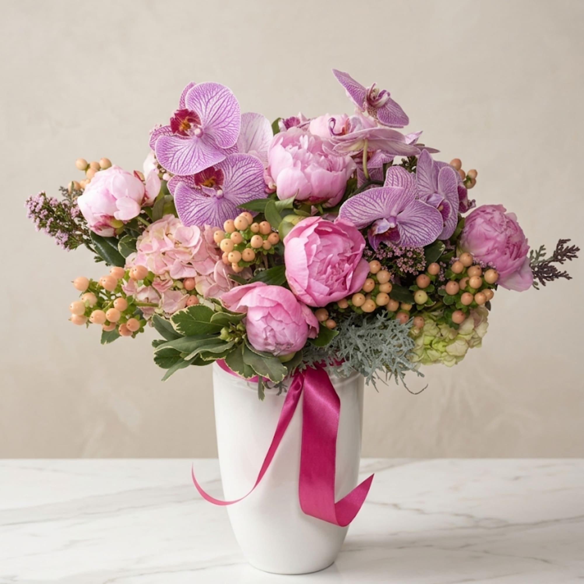 Pink and lavender floral arrangement in a white vase with a magenta ribbon