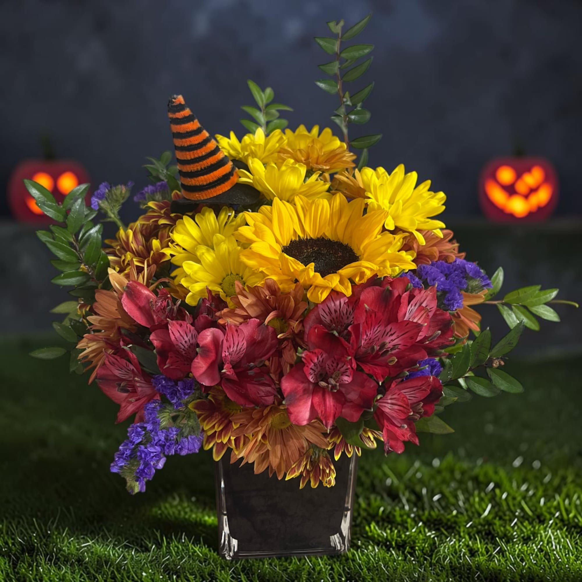 Halloween flower arrangement with sunflowers, red blooms, and a striped witch hat in a vase