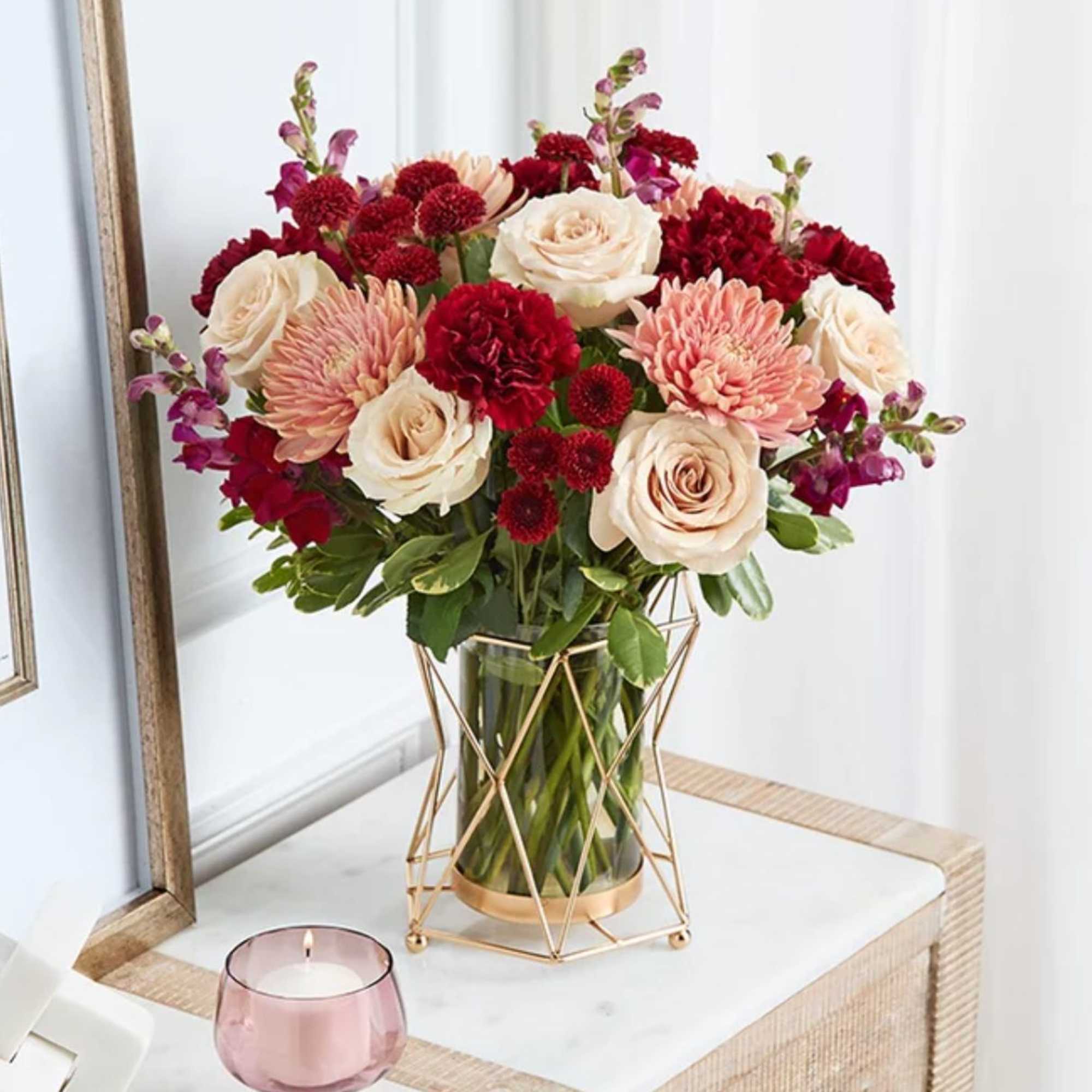 Bouquet of cream roses, red carnations, and pink blooms in a glass vase