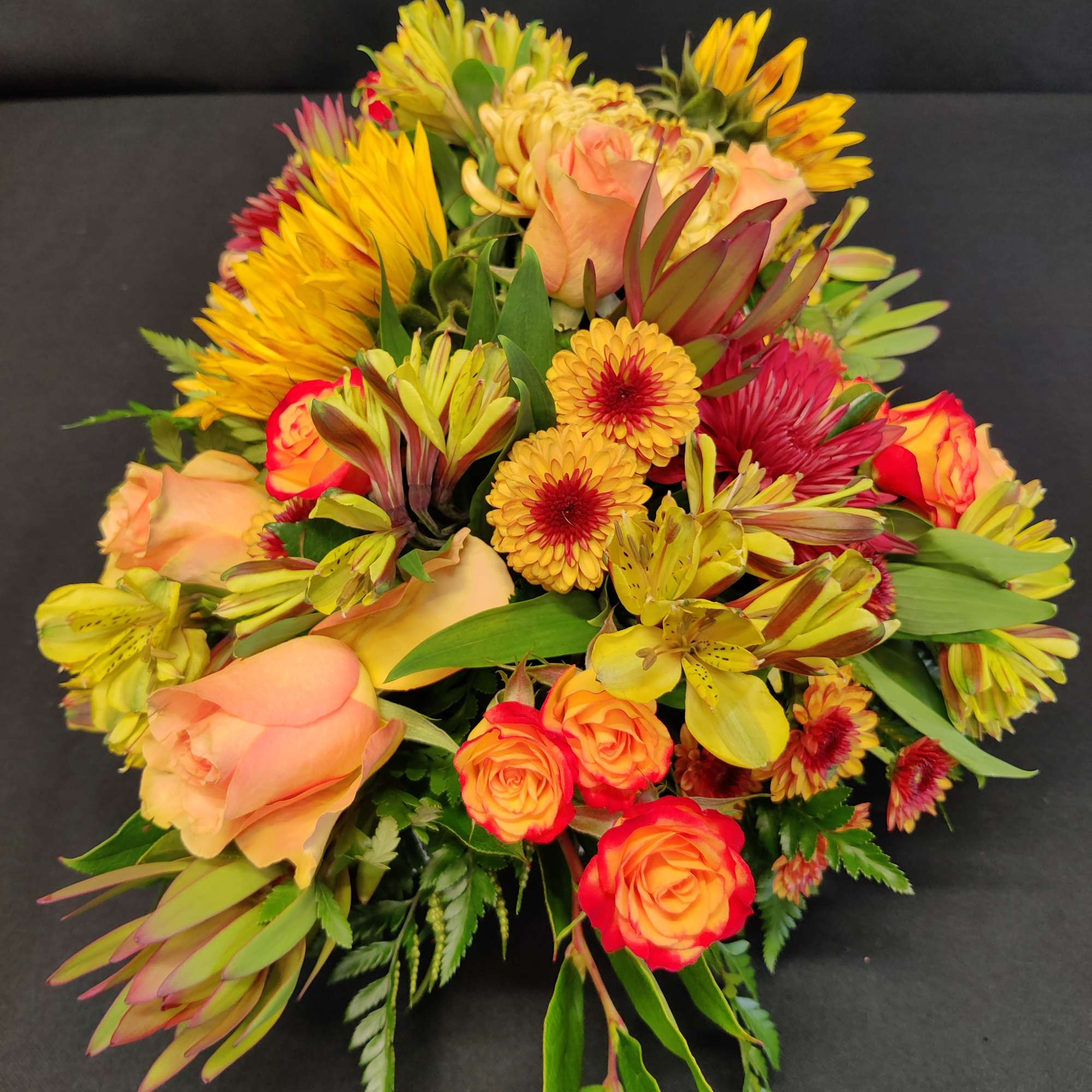 A thickly arranged centerpiece of fall flowers in a low design dish., photo 4 of 4