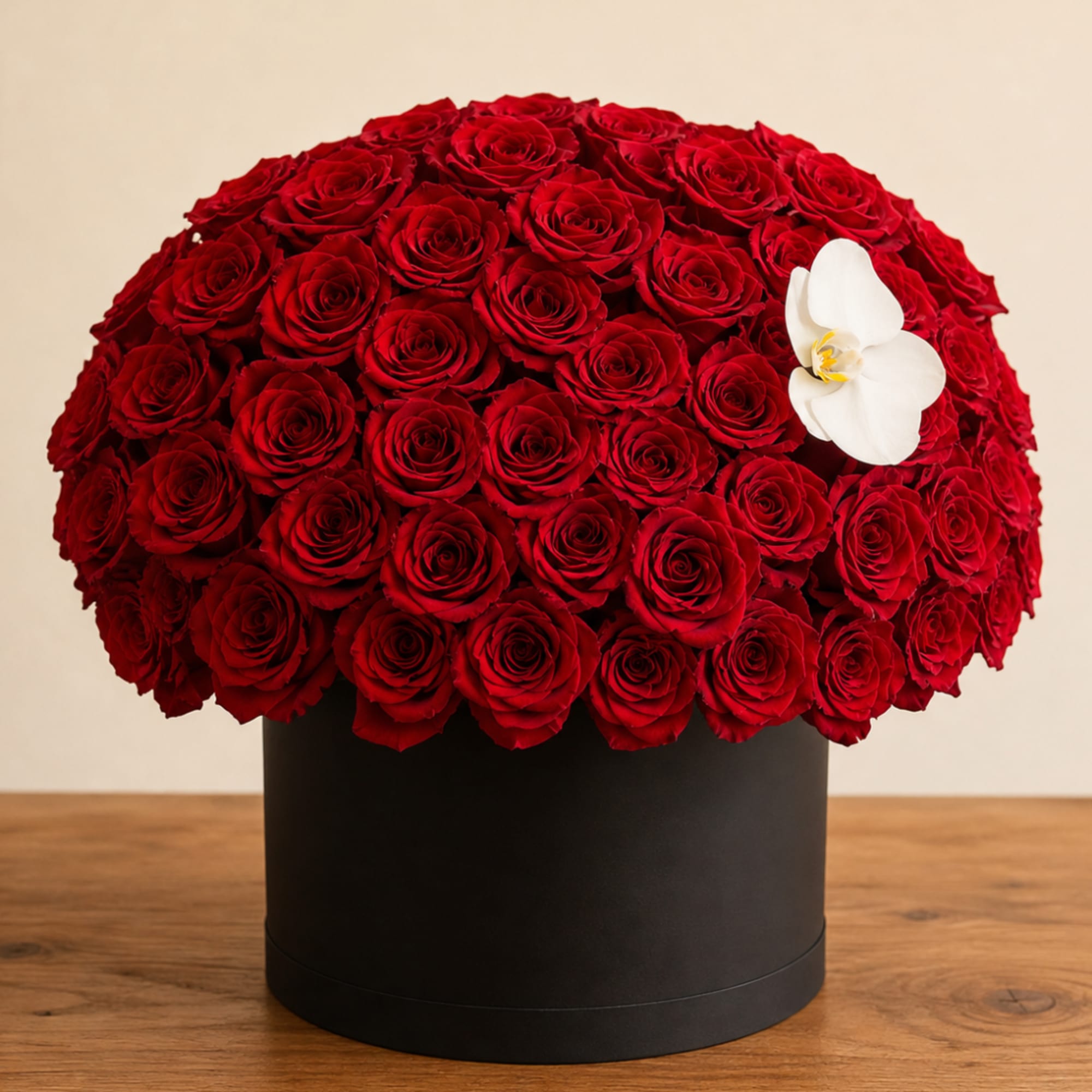 Round arrangement of red roses in a black box with a white orchid accent