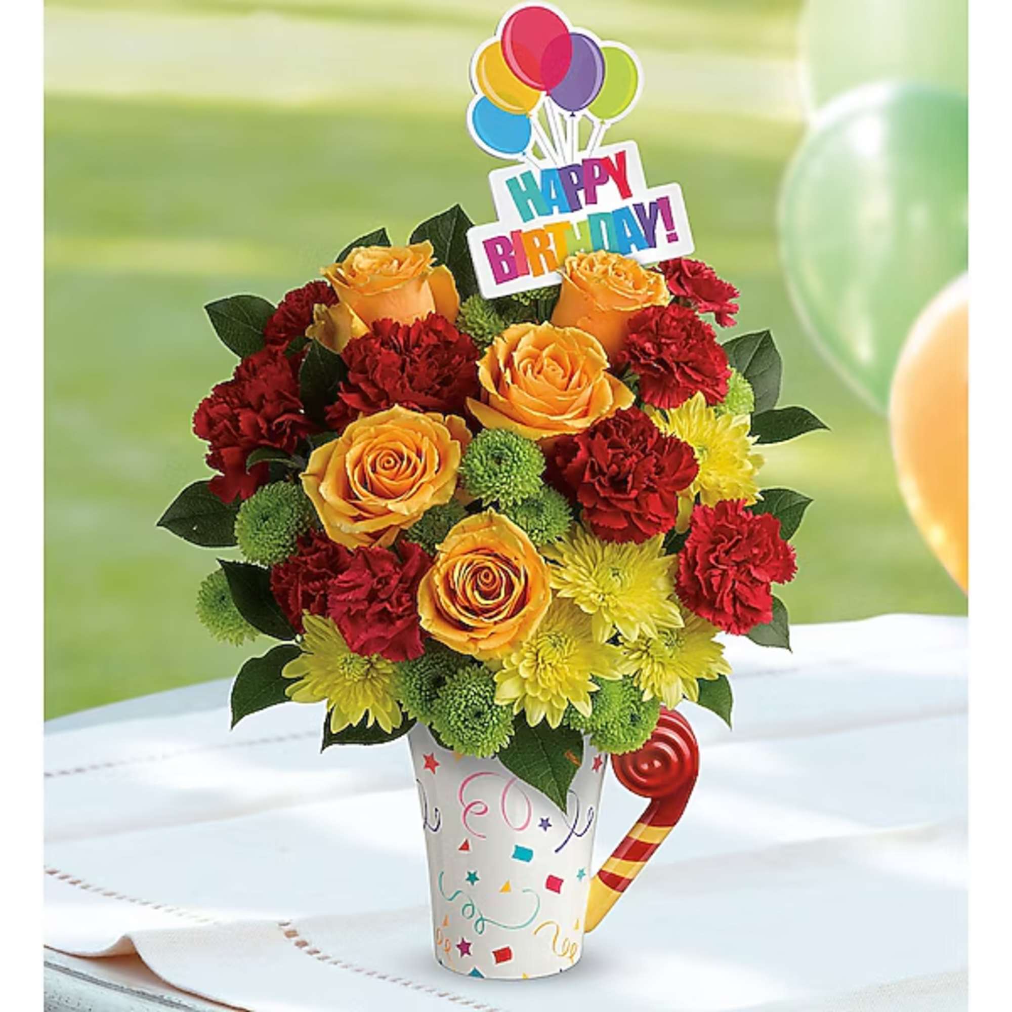 Birthday bouquet of orange roses, red carnations, and yellow mums in a party mug