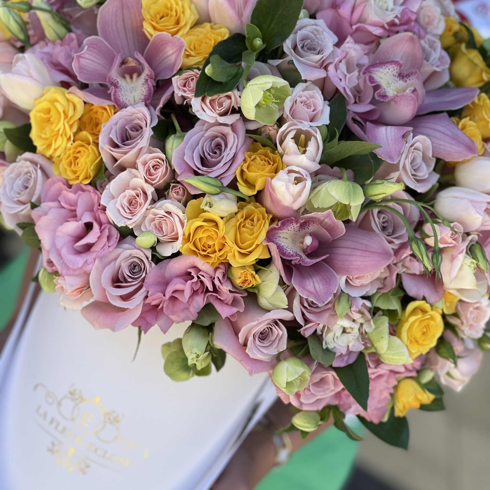 Bouquet of pink and yellow roses with orchids in a white box