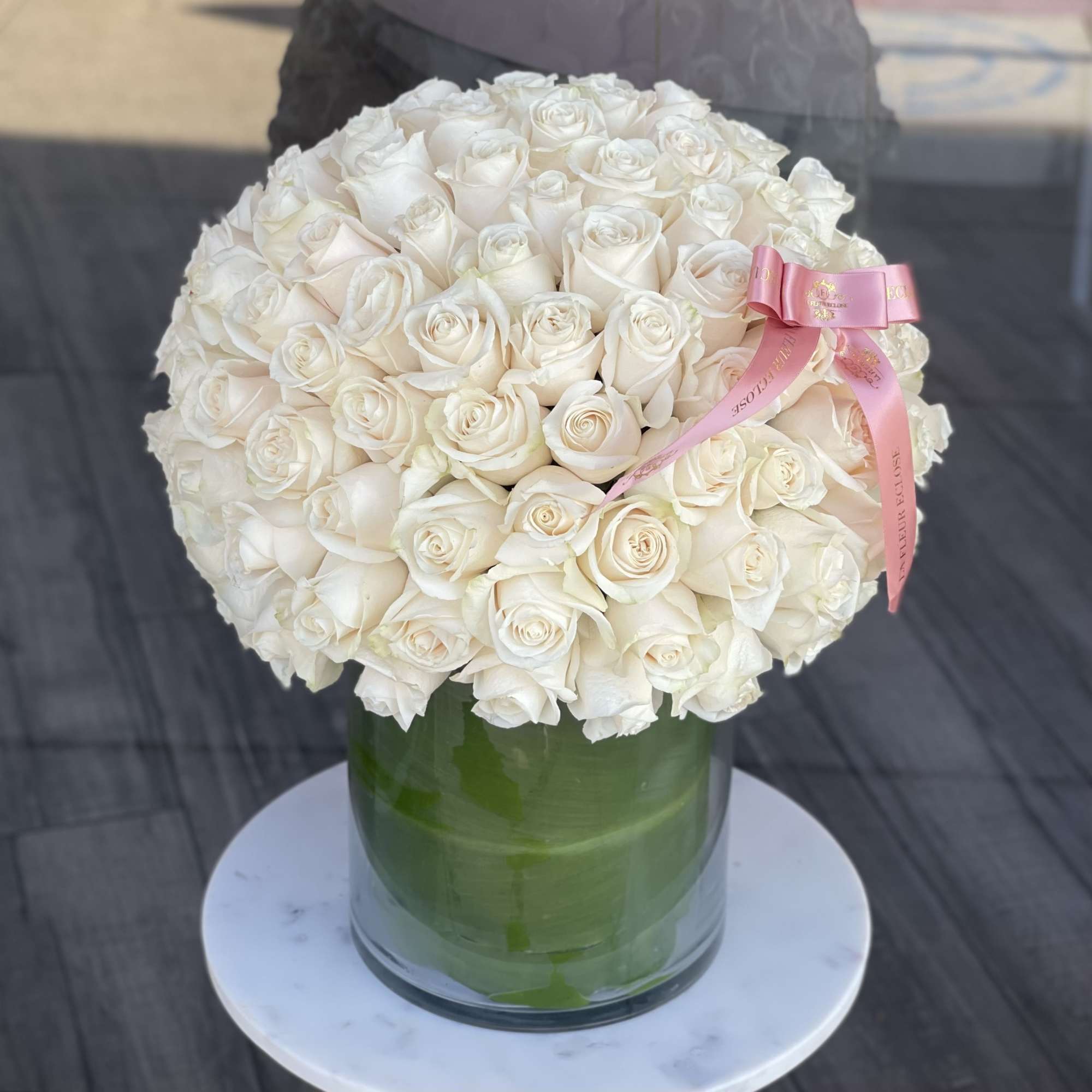 Large bouquet of white roses in a glass vase with a pink ribbon