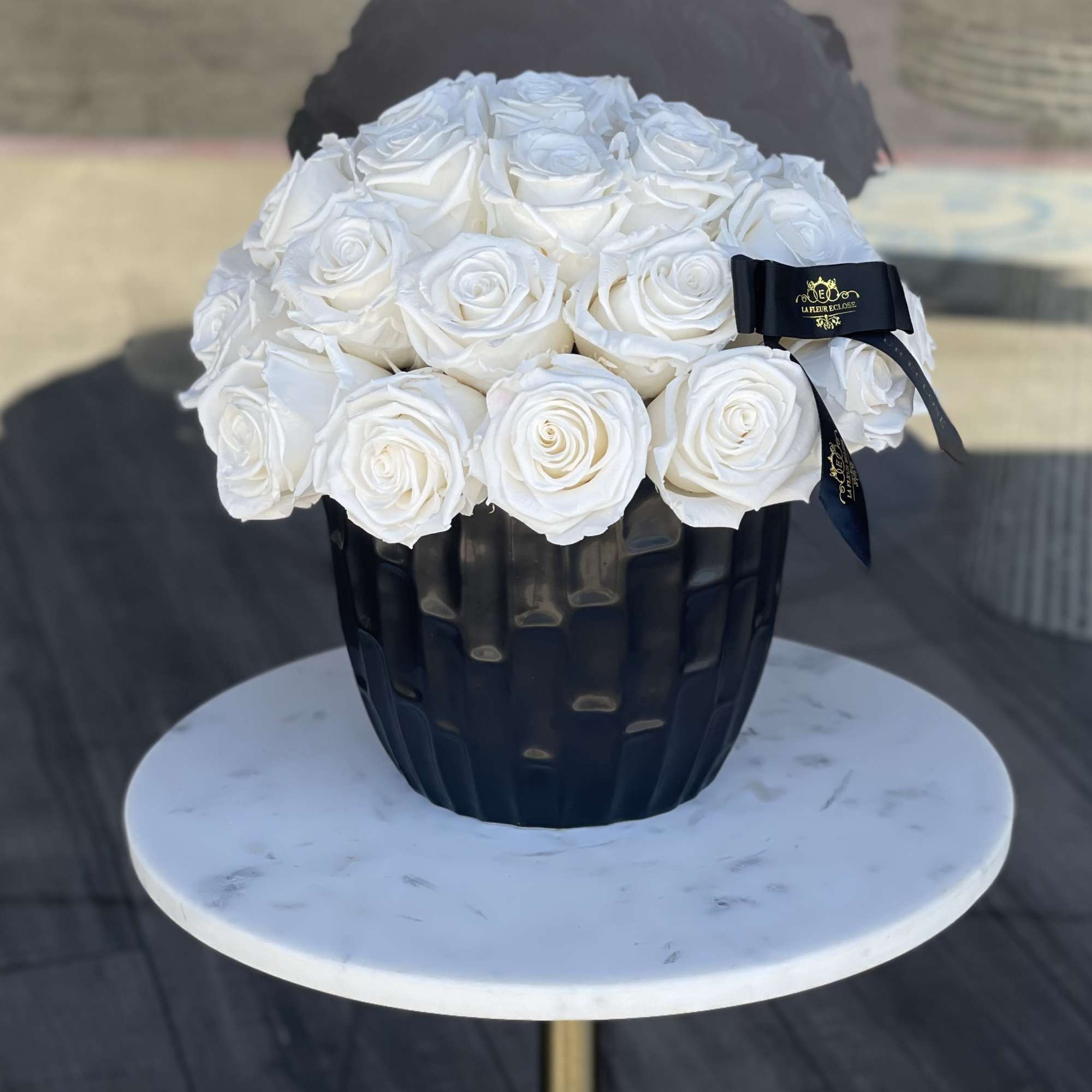 White roses arranged in a black vase with a ribbon bow