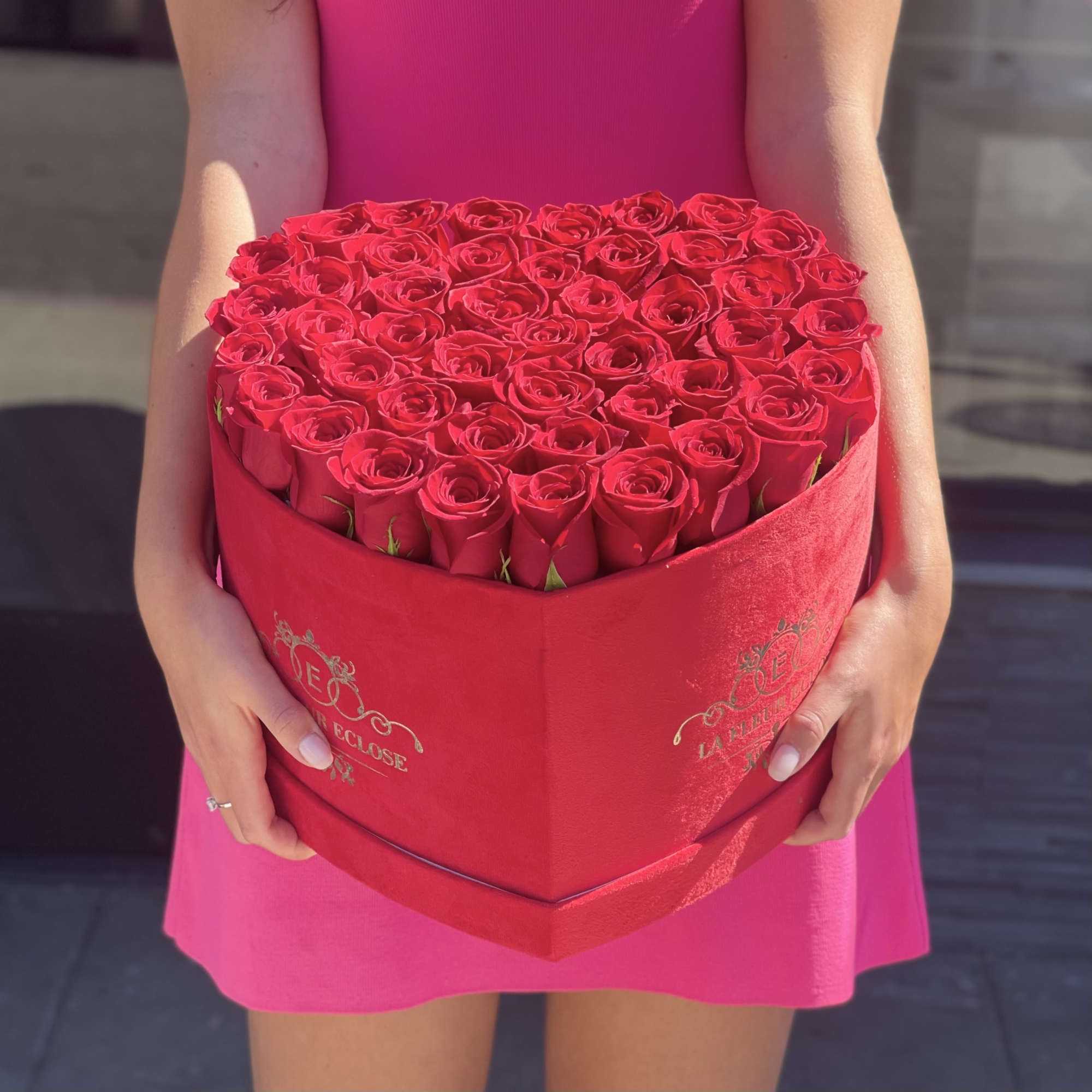 Heart-shaped box of red roses held by a person in a pink dress