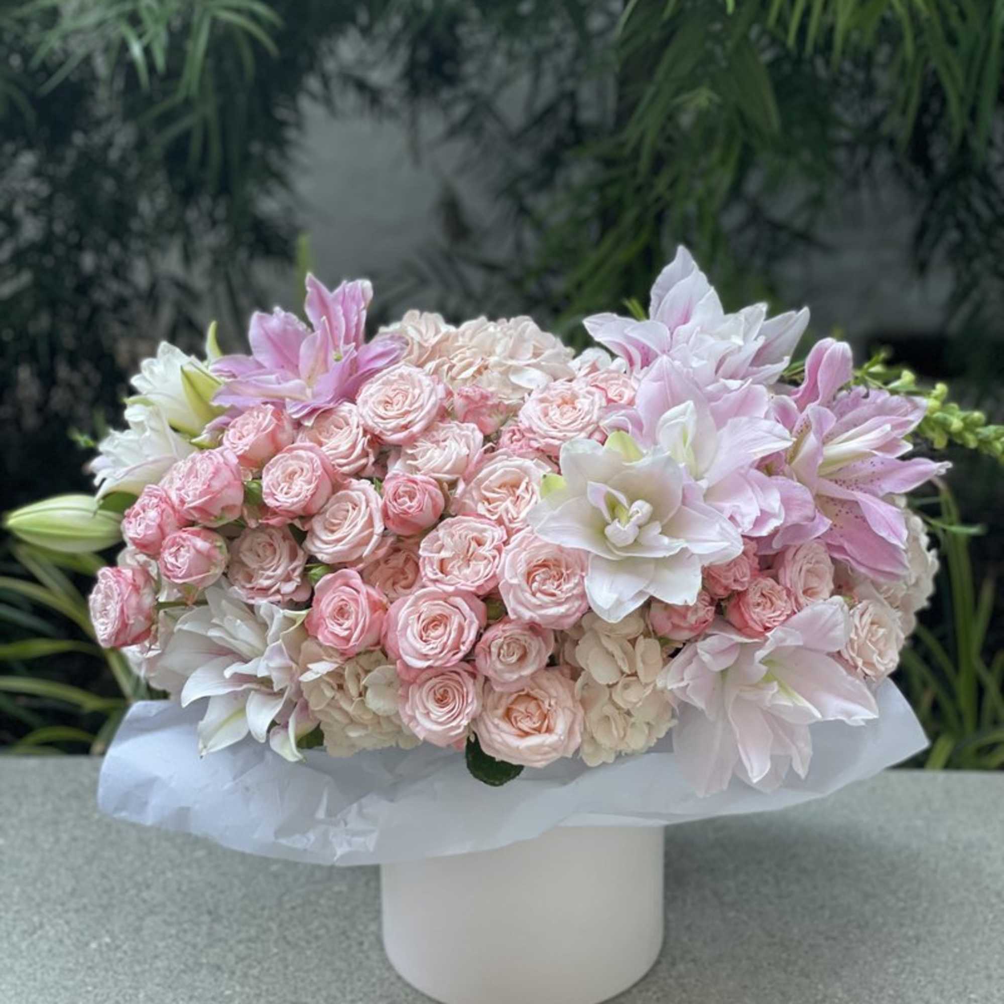 Pink roses and white lilies arranged in a white box vase