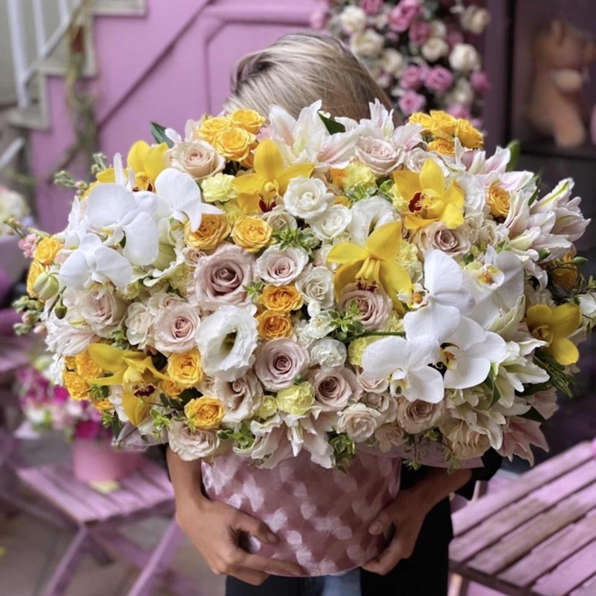Large bouquet of white, yellow, and blush flowers held in a pink box