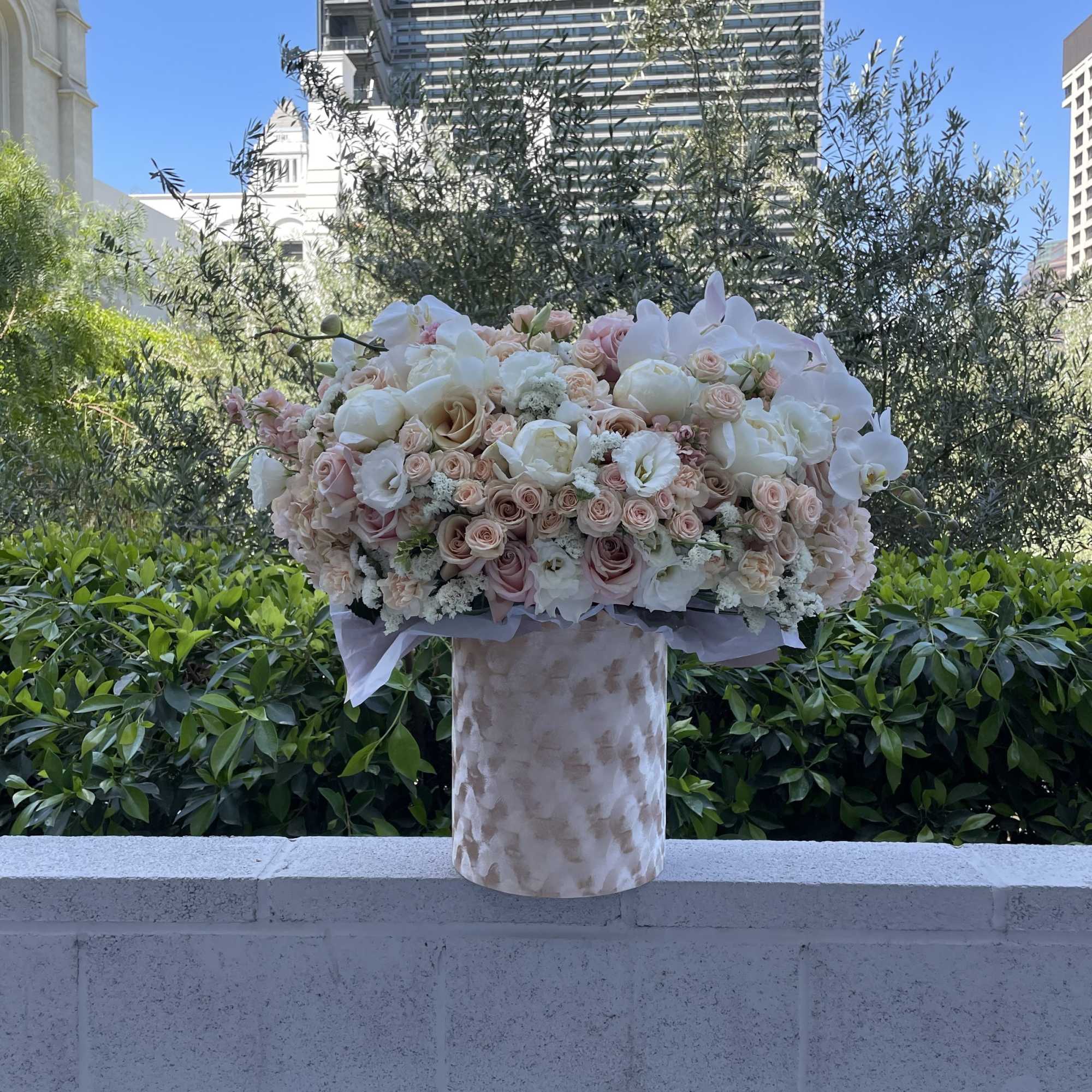 Large blush and white floral arrangement in a patterned vase outdoors
