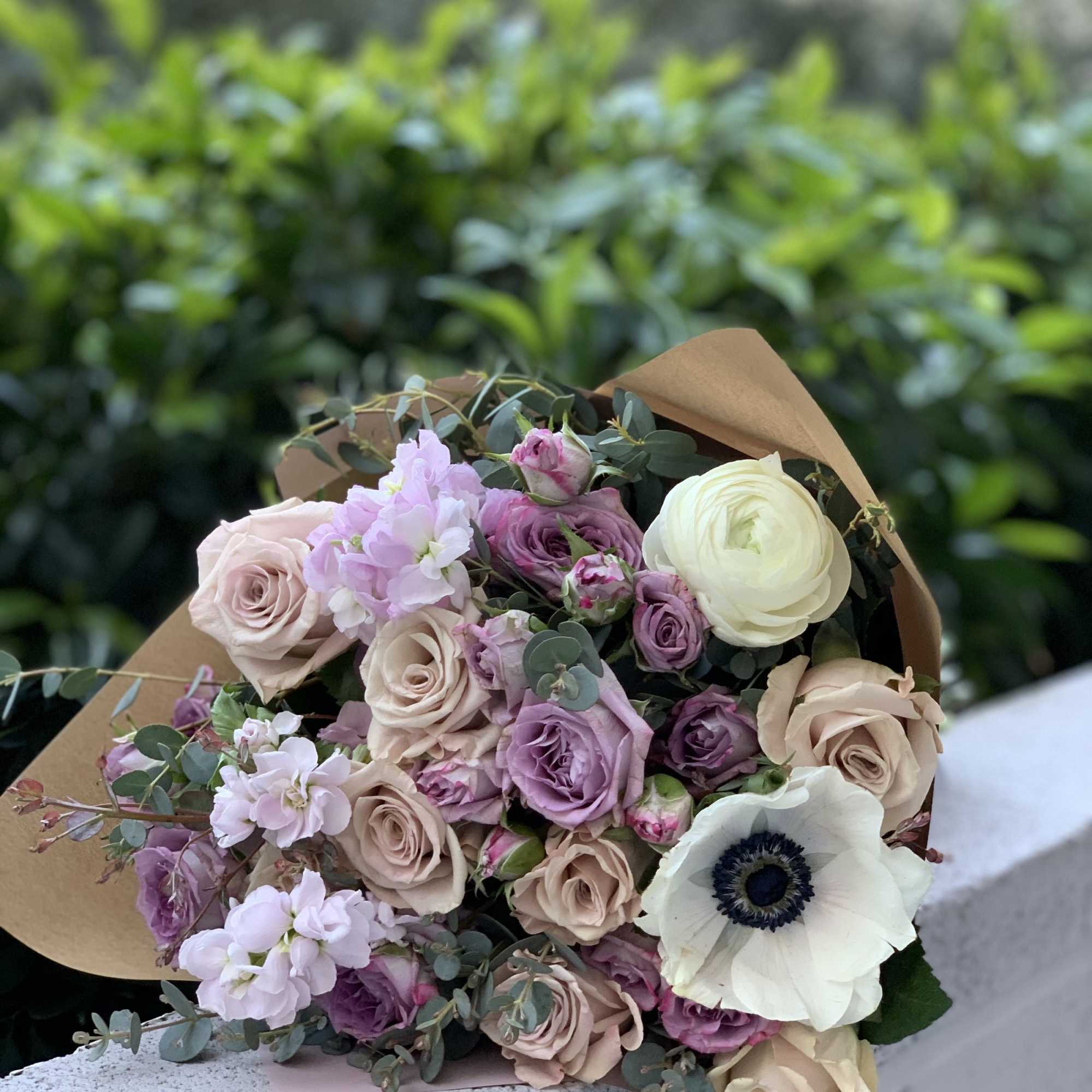 Bouquet of blush, lavender, and white flowers wrapped in brown paper
