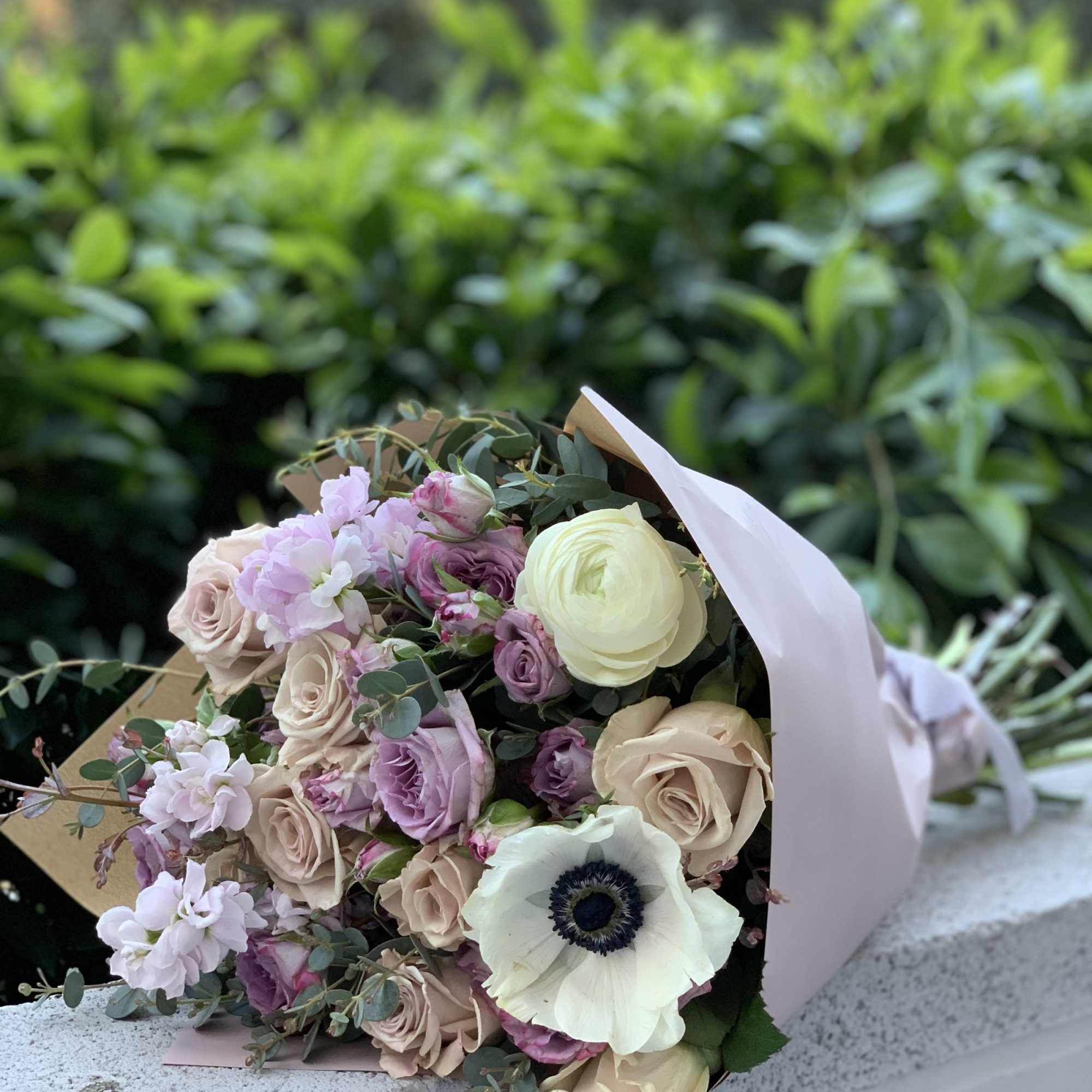 Bouquet of pale roses, lavender blooms, and a white anemone wrapped in paper