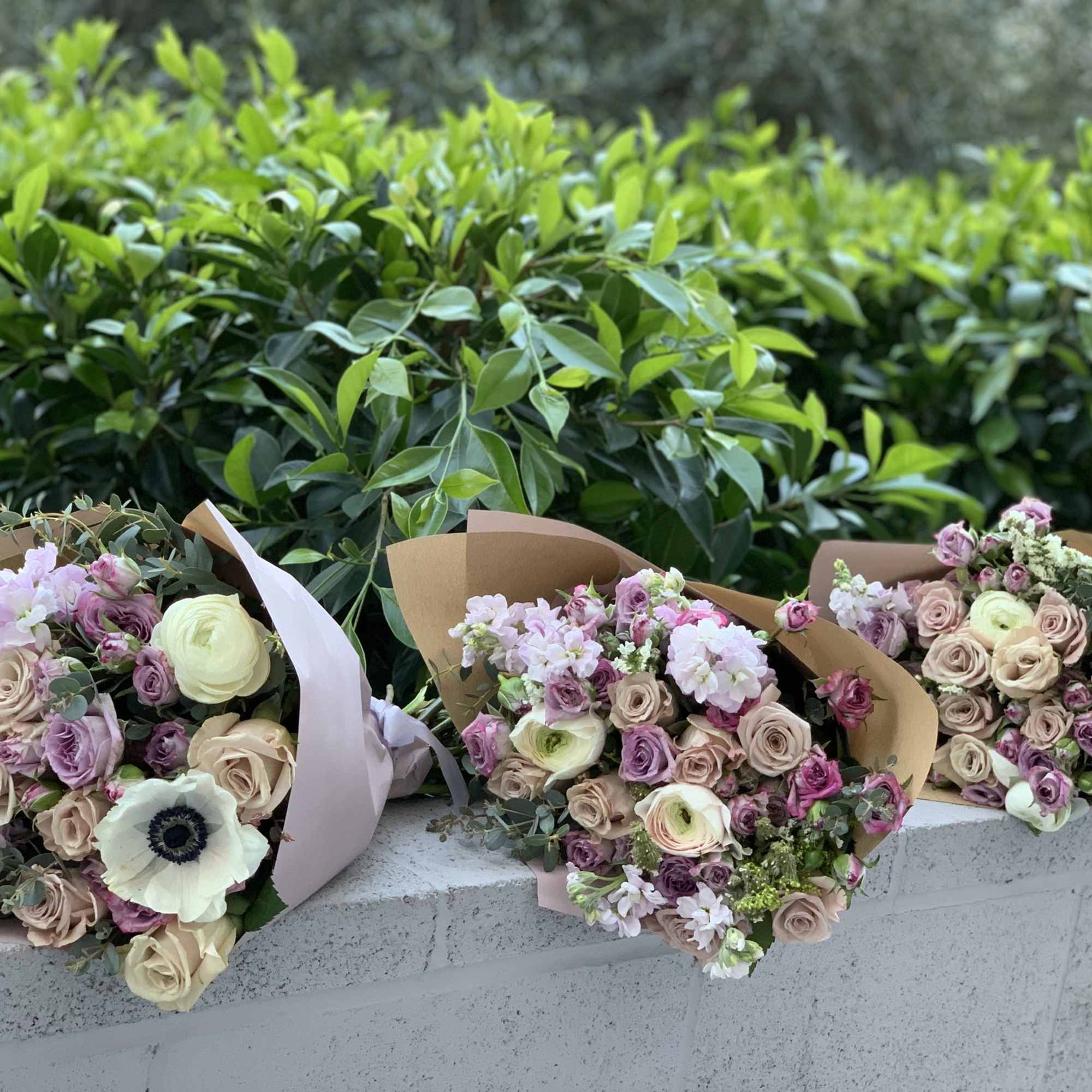 Three pastel bouquets wrapped in brown paper and resting on a ledge.