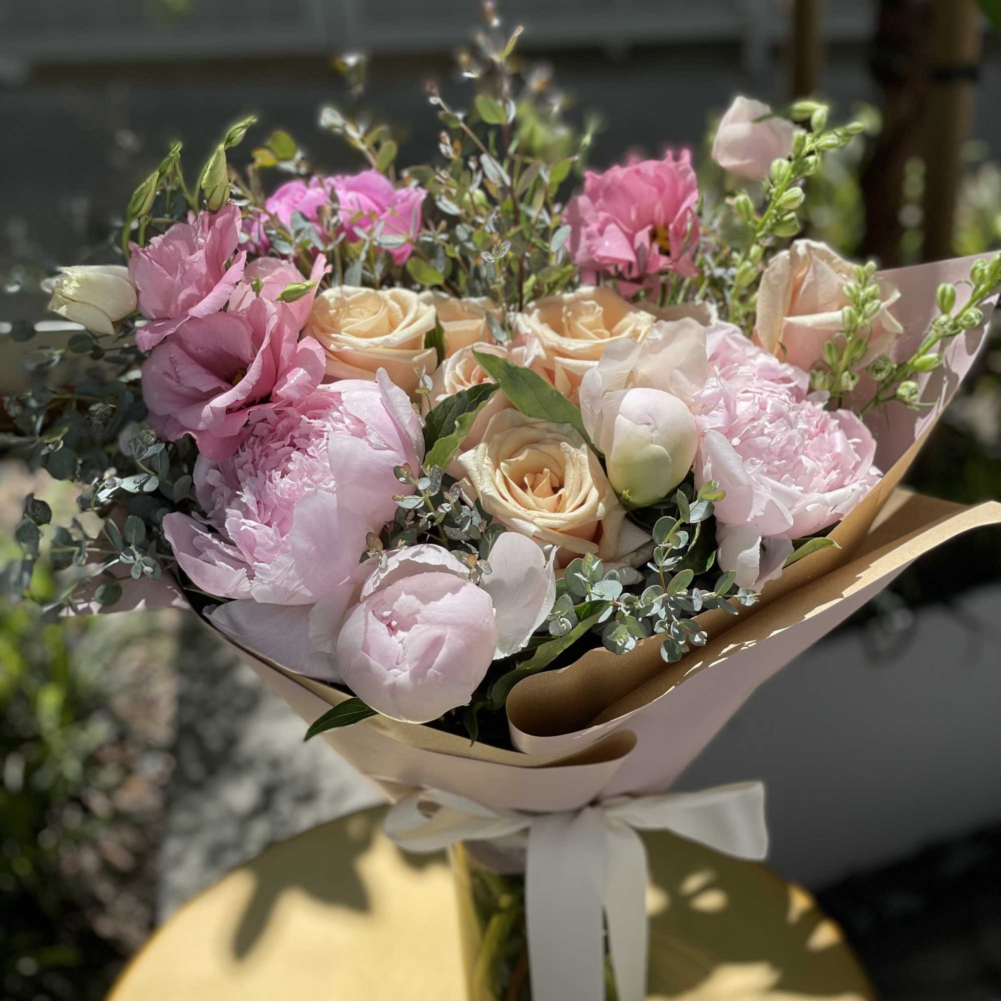 Bouquet of pink and cream roses and peonies wrapped in paper