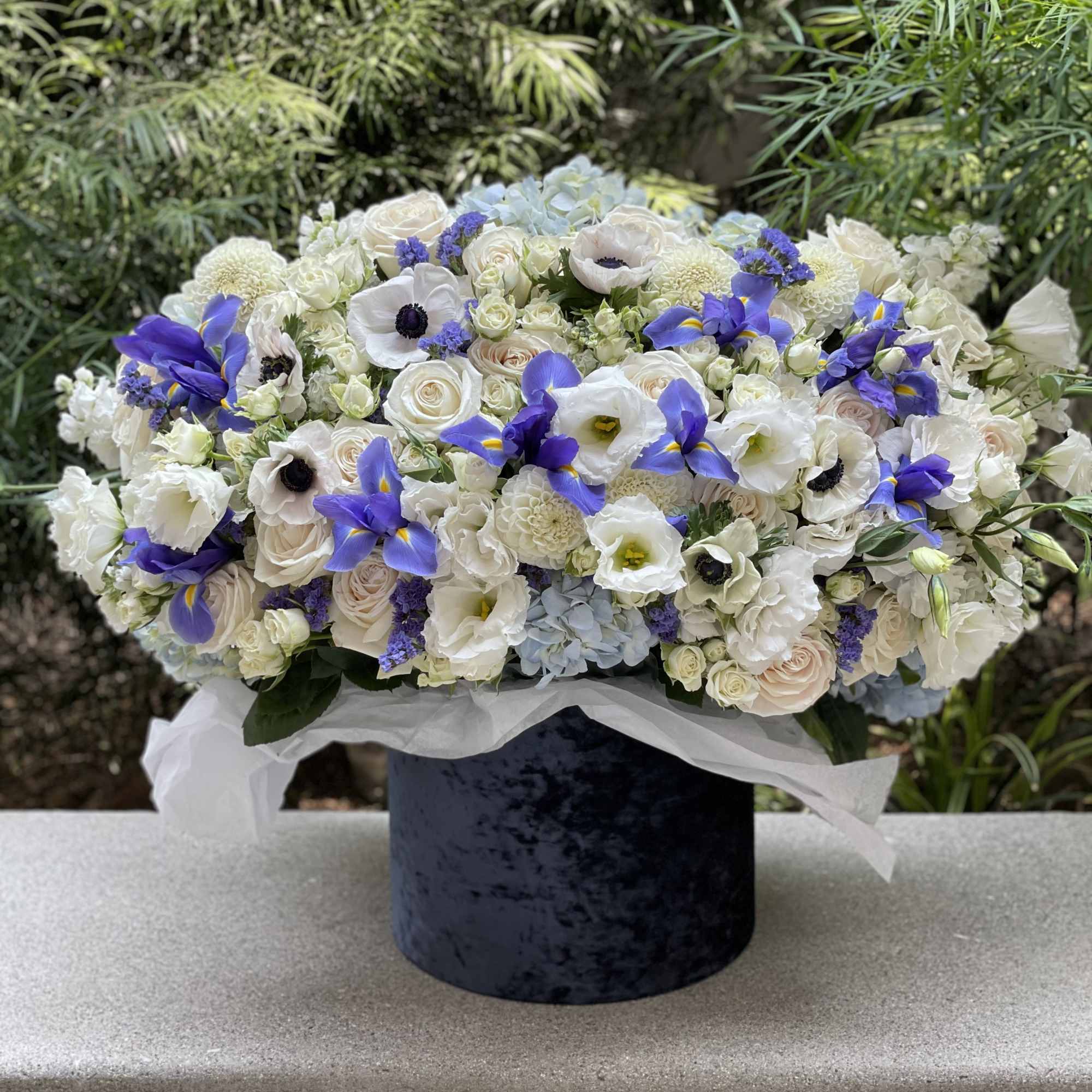 Large white and blue floral arrangement in a dark velvet box