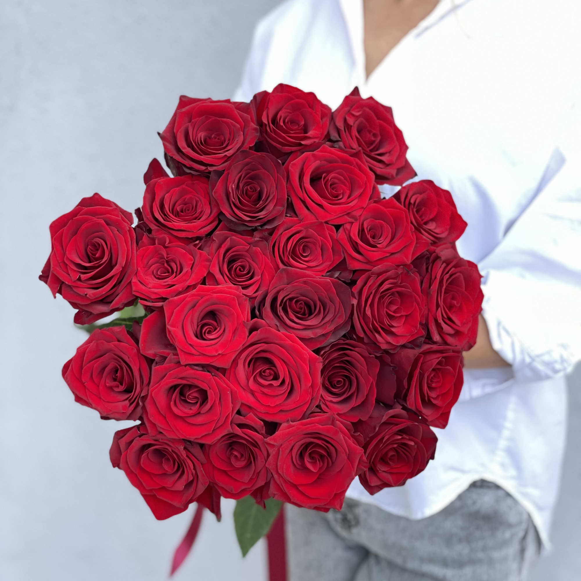 Bouquet of red roses held by a person in a white shirt
