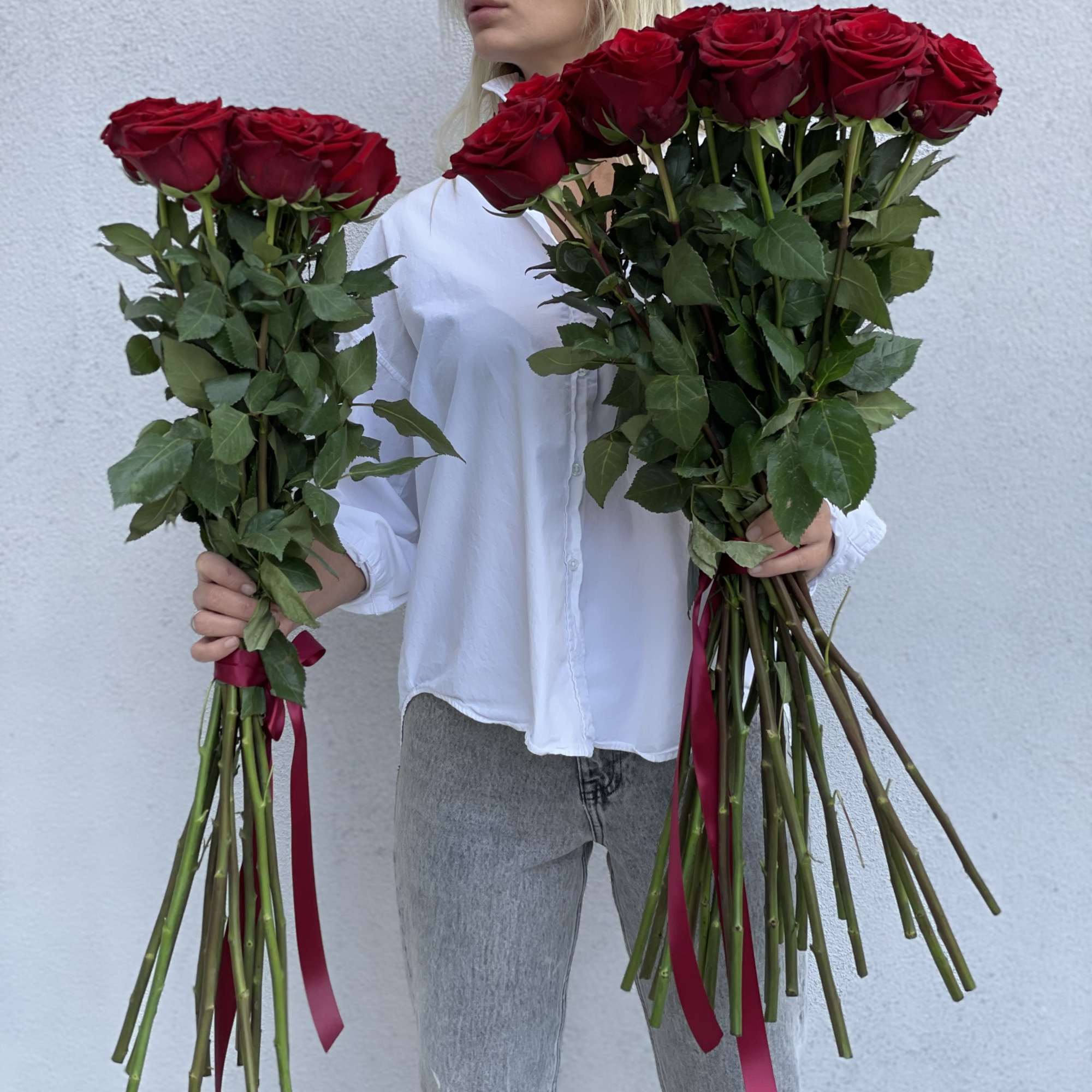 Person holding two long-stemmed bouquets of red roses