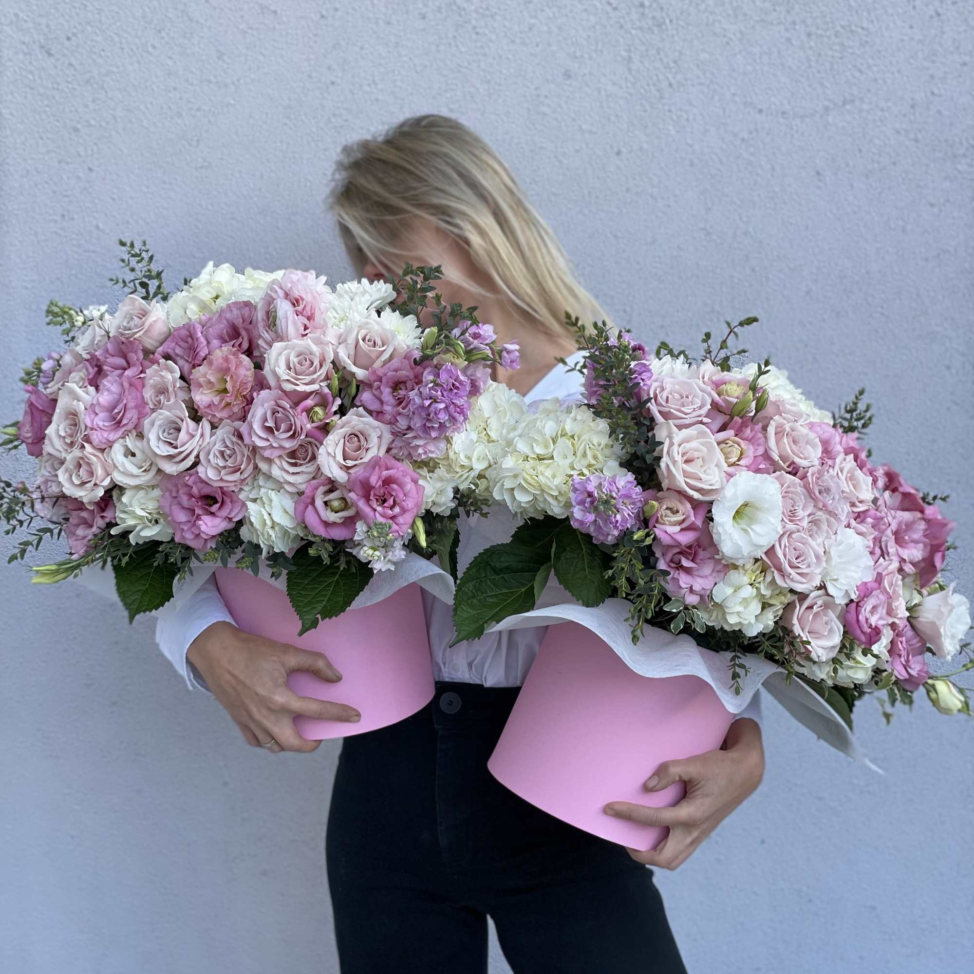 Woman holding two large pink flower boxes filled with roses and hydrangeas