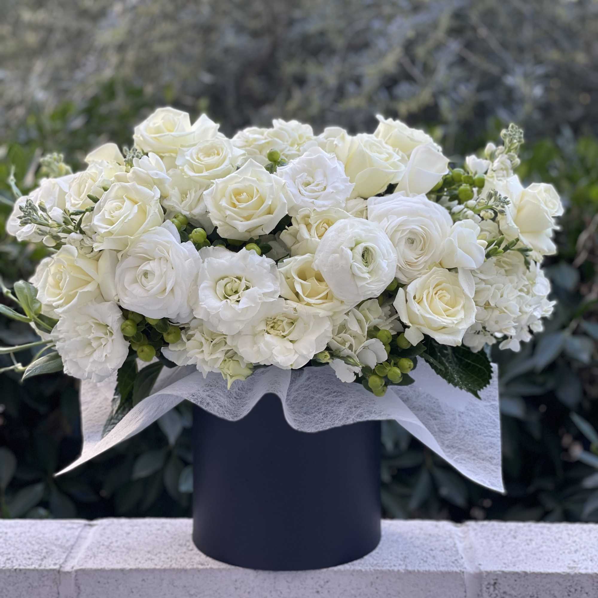 White rose and ranunculus arrangement in a black hat box