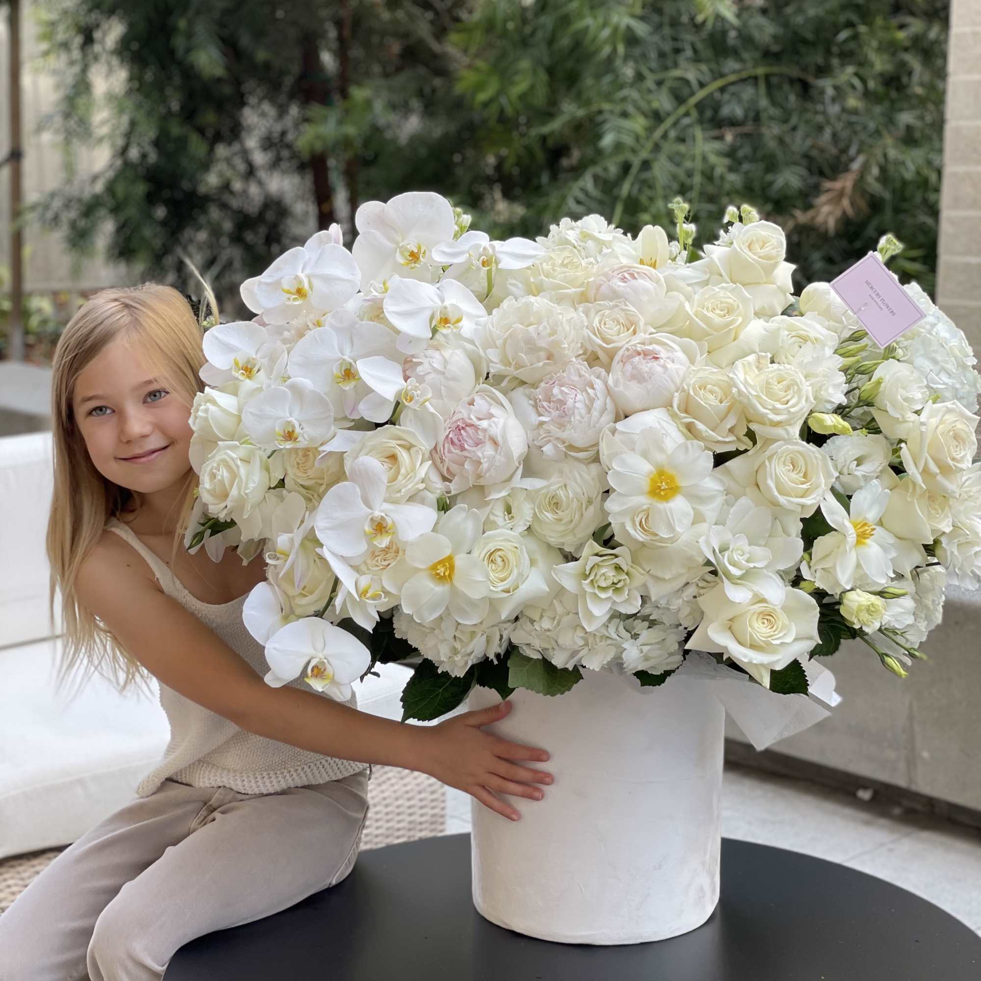 Large white floral arrangement in a white cylinder vase
