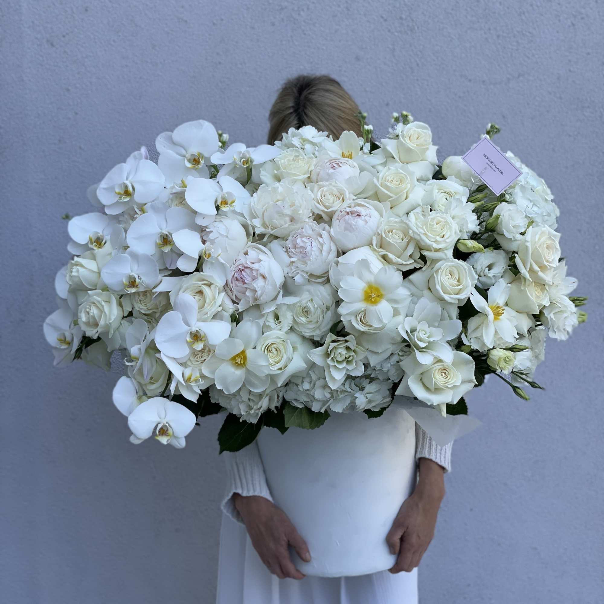 Large white floral arrangement in a white container held by a person