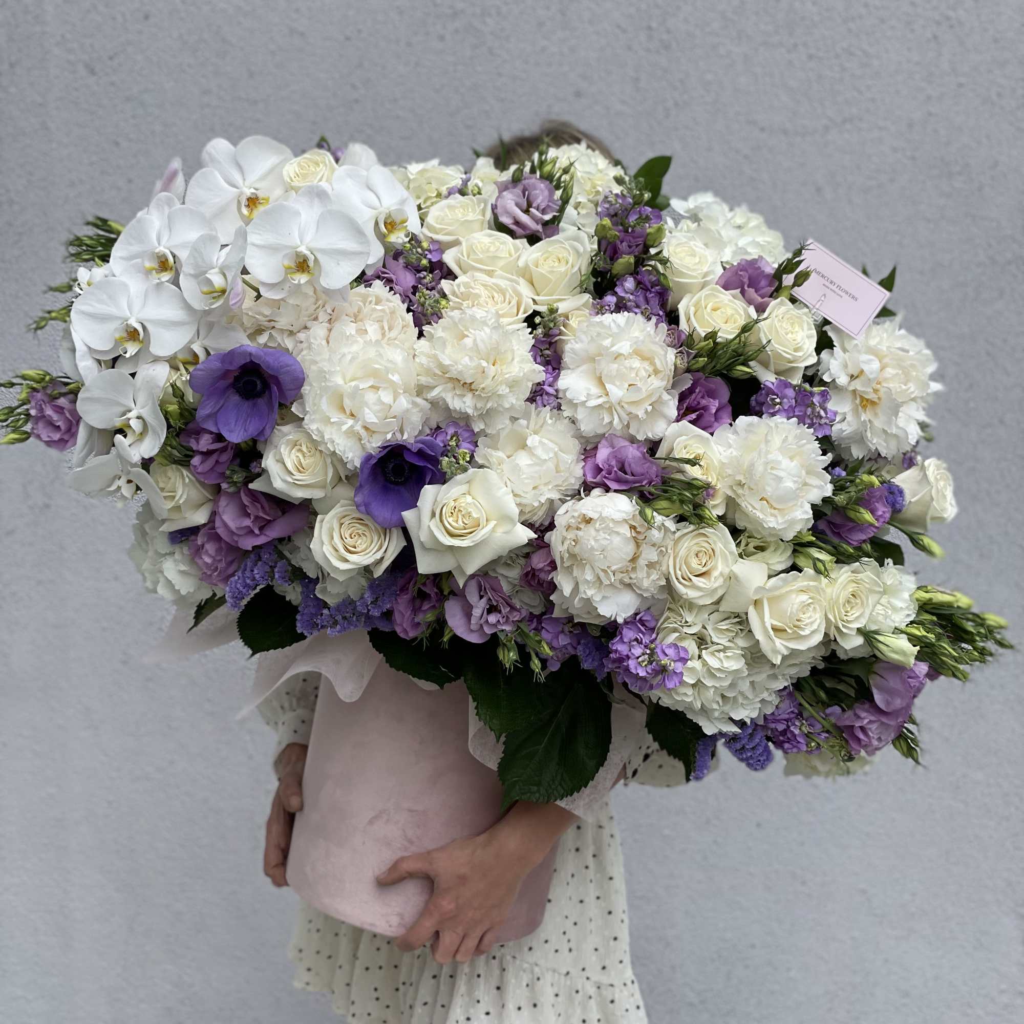 Large bouquet of white and purple flowers wrapped in pale pink paper