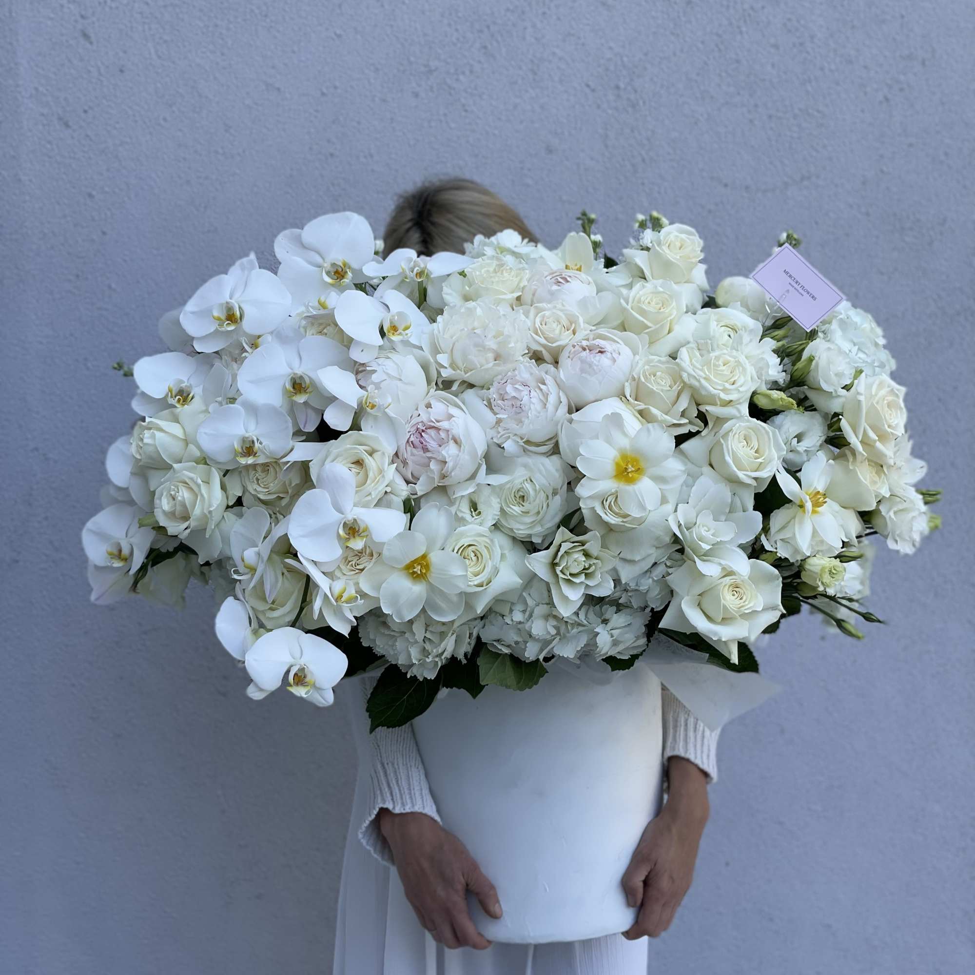 Large white bouquet with roses and orchids in a white container