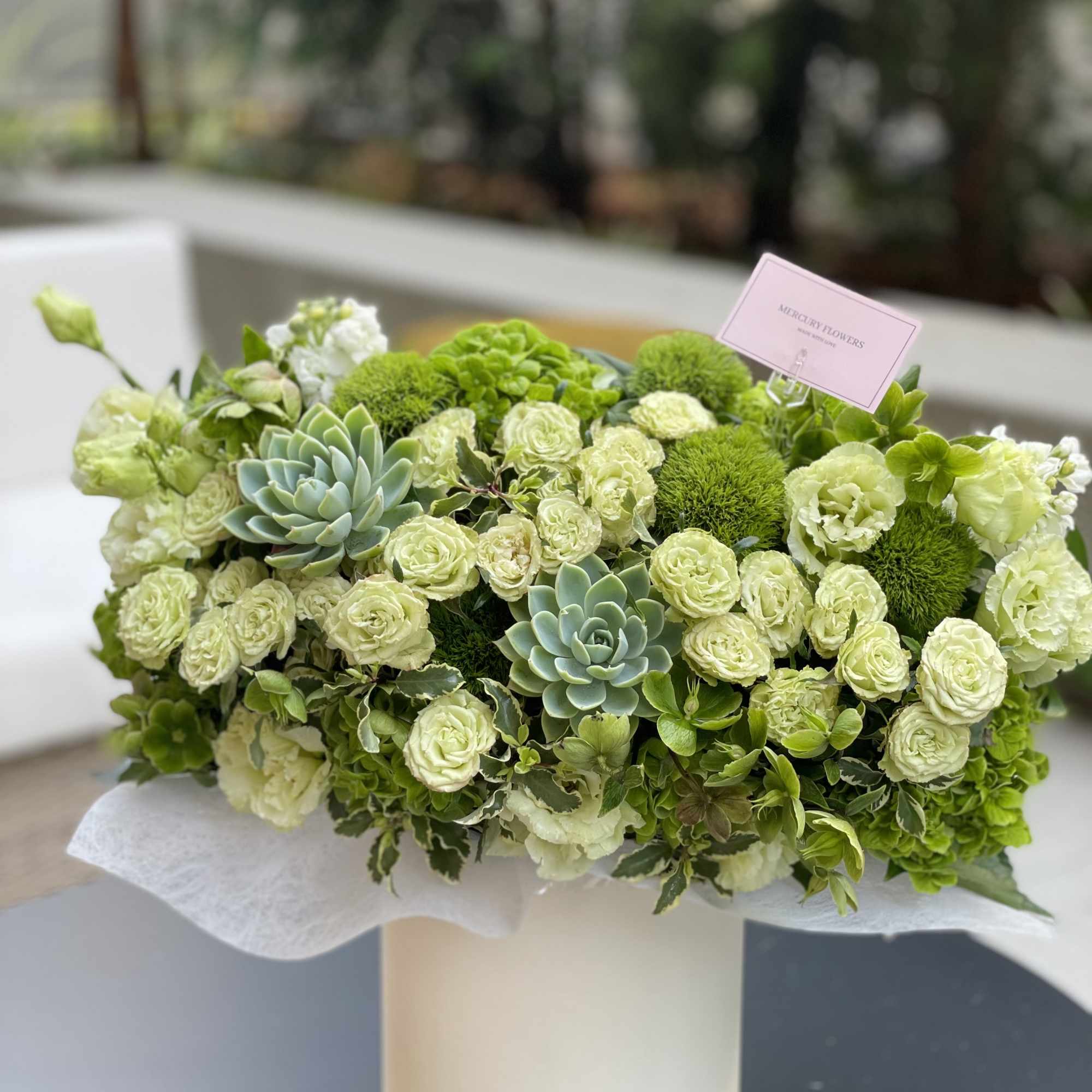 Green and white floral arrangement with succulents in a white box