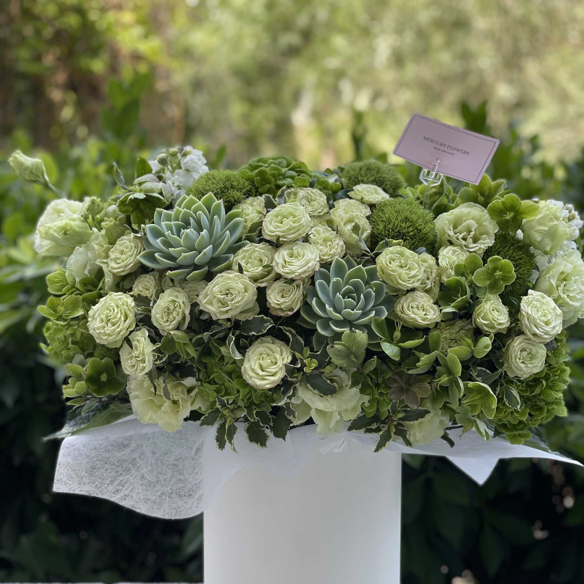 Green and white floral arrangement in a white vase with succulents