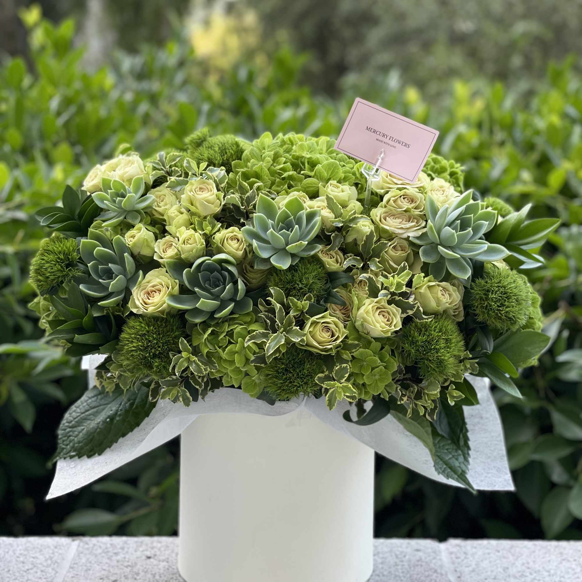 Green and cream floral arrangement in a white box with succulents and roses