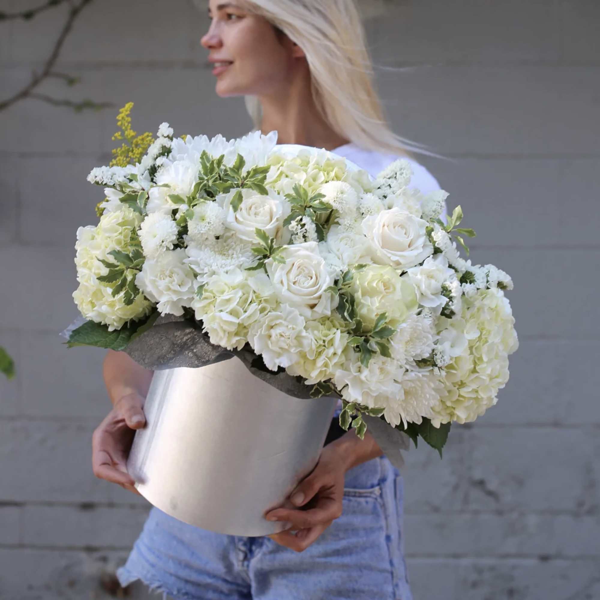 Woman holding a large white floral arrangement in a silver box
