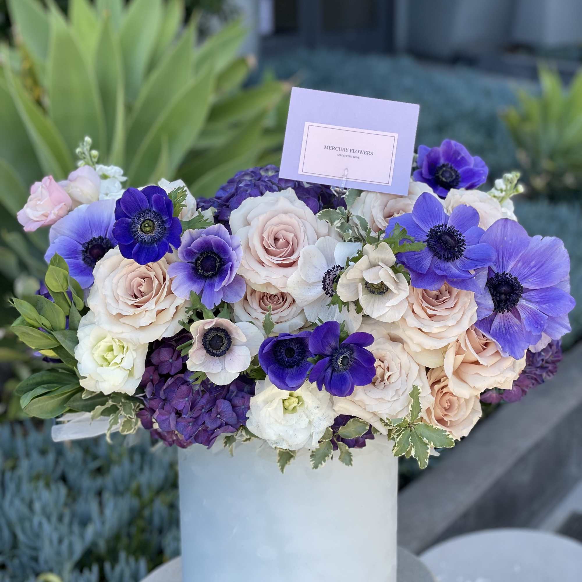 Bouquet of blush roses and purple anemones in a white vase