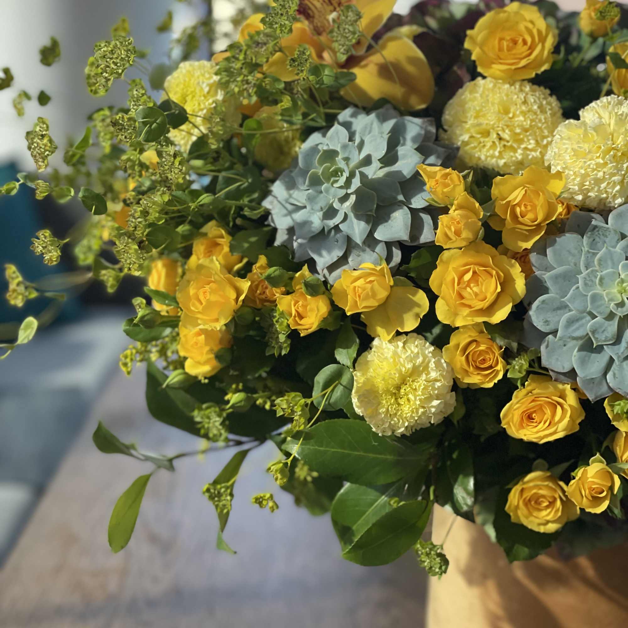 Yellow roses and pale blooms arranged with blue-green succulents