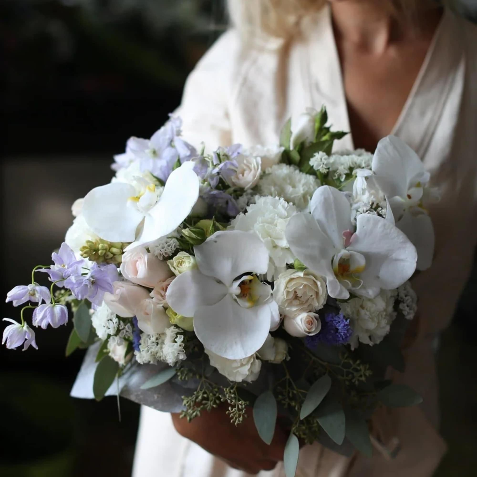 Woman holding a bouquet of white orchids and pale flowers