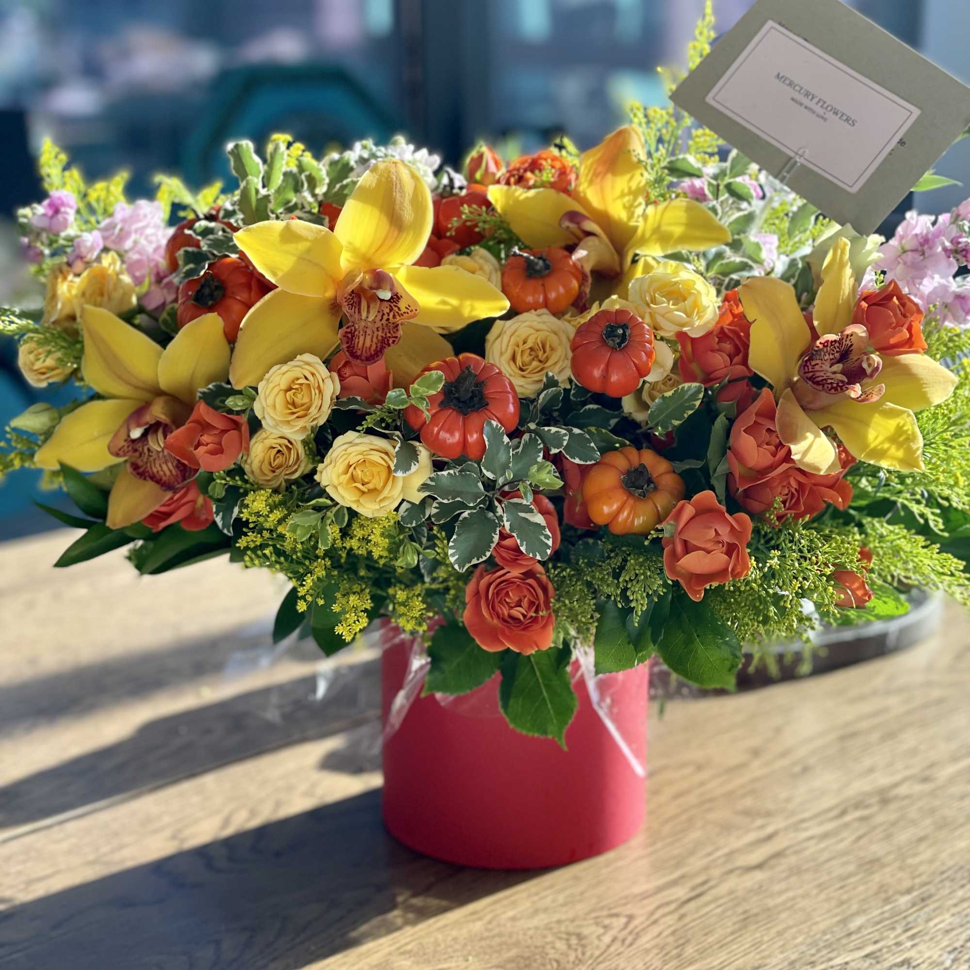 Bright mixed flower arrangement in a pink vase with yellow orchids and roses