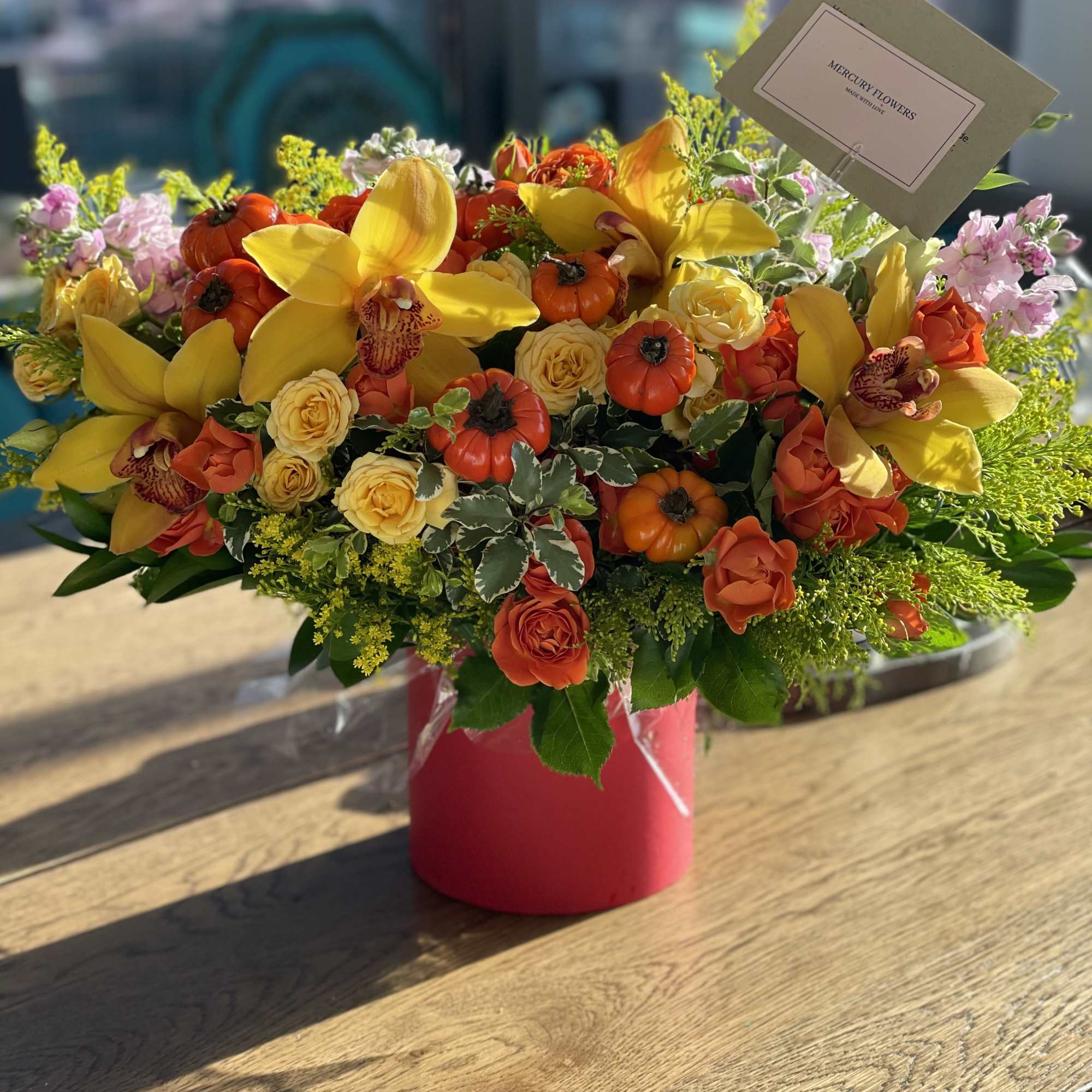 Yellow orchids and orange roses in a pink vase with small pumpkins