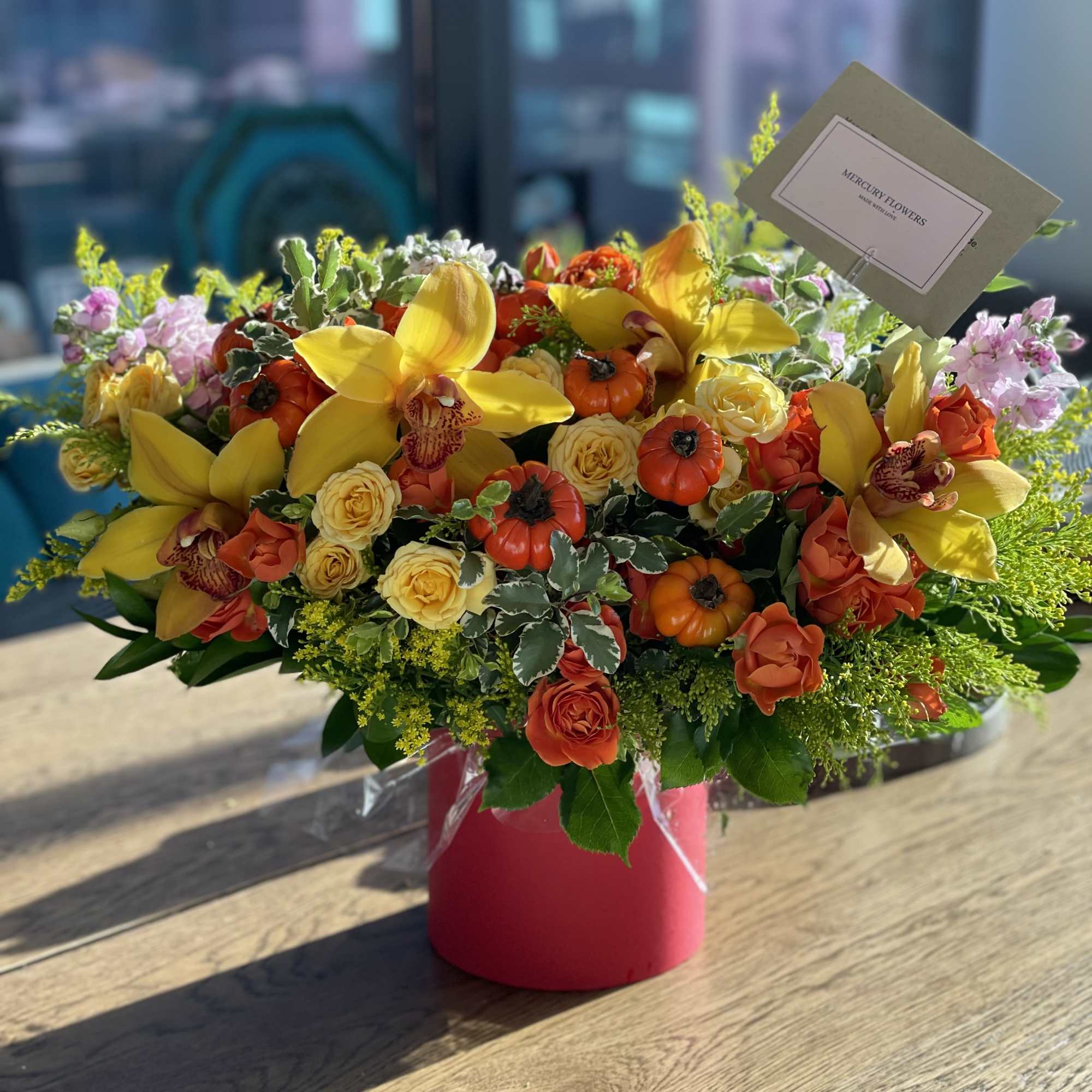 Bright mixed flower arrangement in a pink box with yellow orchids and roses