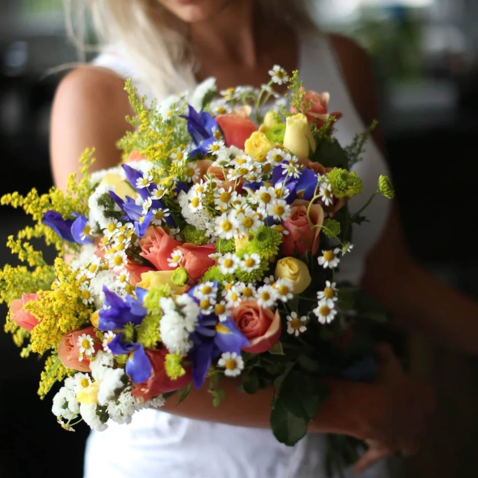 Woman holding a colorful mixed bouquet of roses and daisies