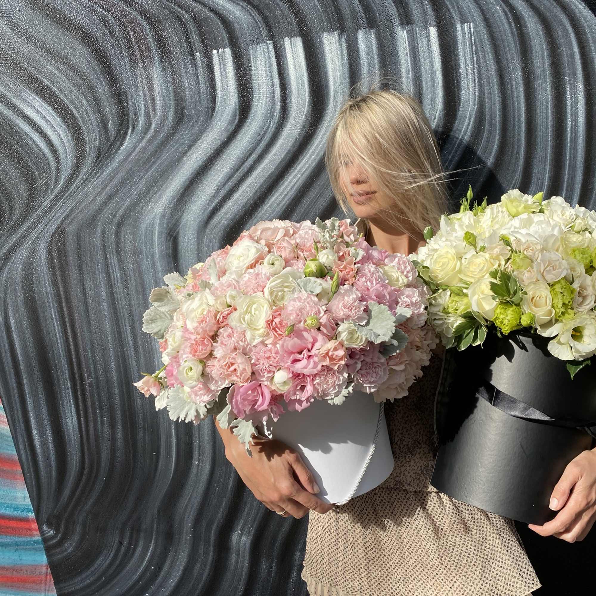 Woman holding two large pastel flower arrangements in round boxes