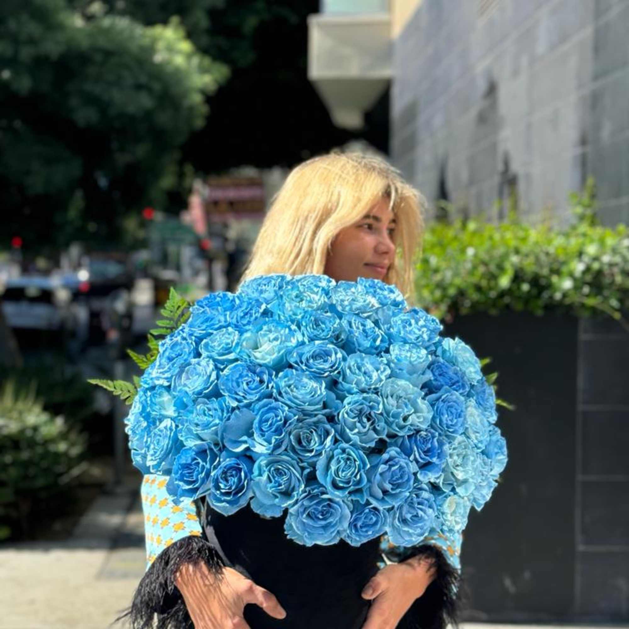 Woman holding a large bouquet of bright blue roses in a black vase