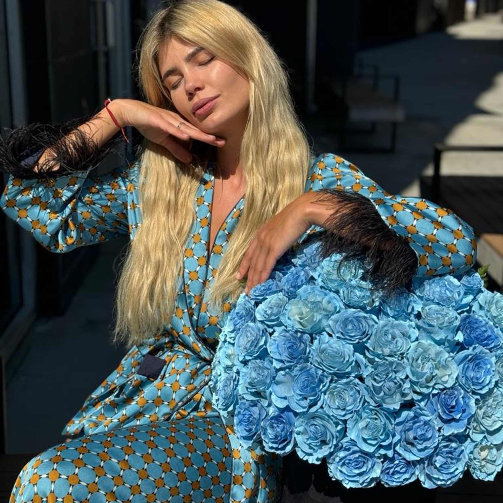 Woman posing beside a large blue rose arrangement in a black box