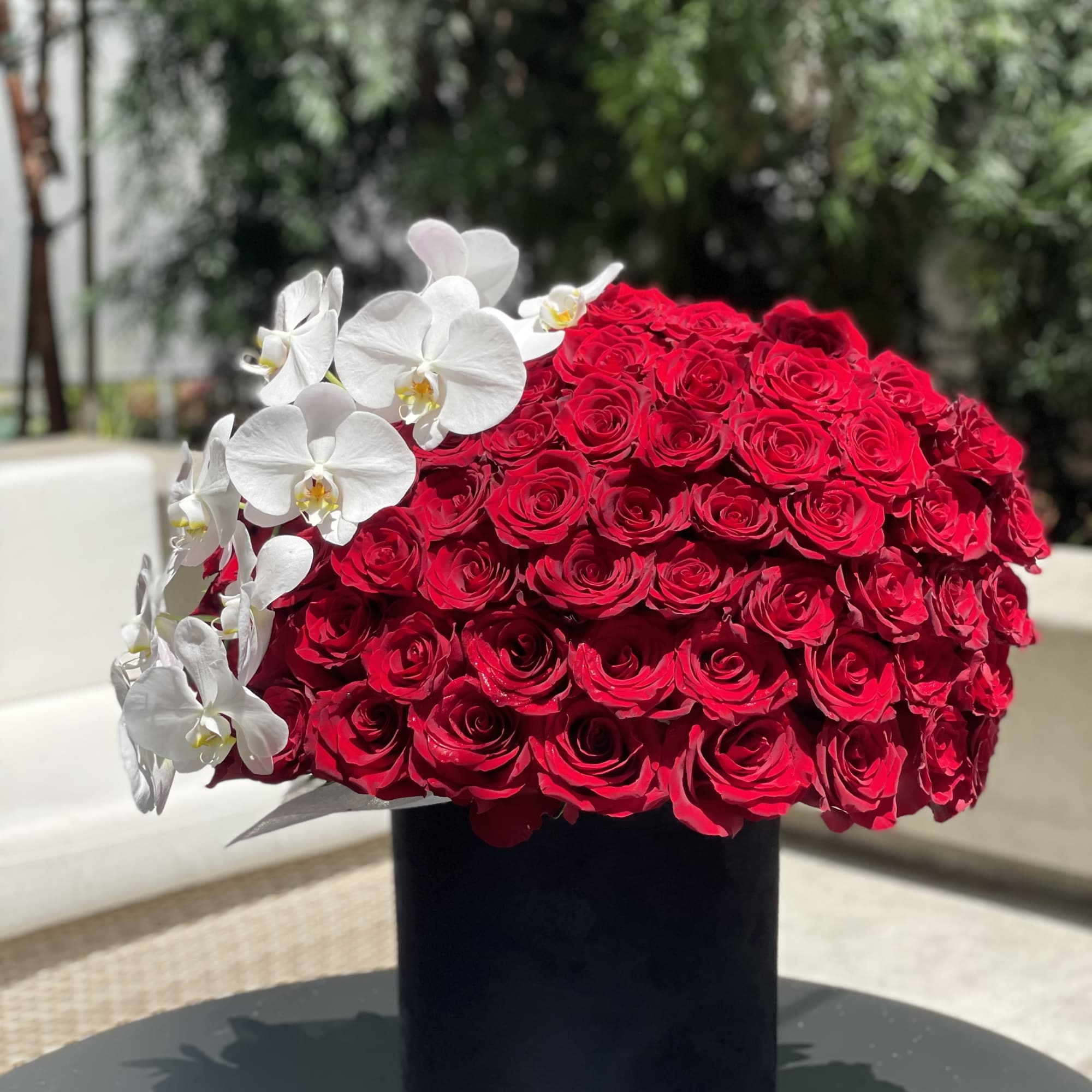 Large red rose arrangement with white orchids in a black vase