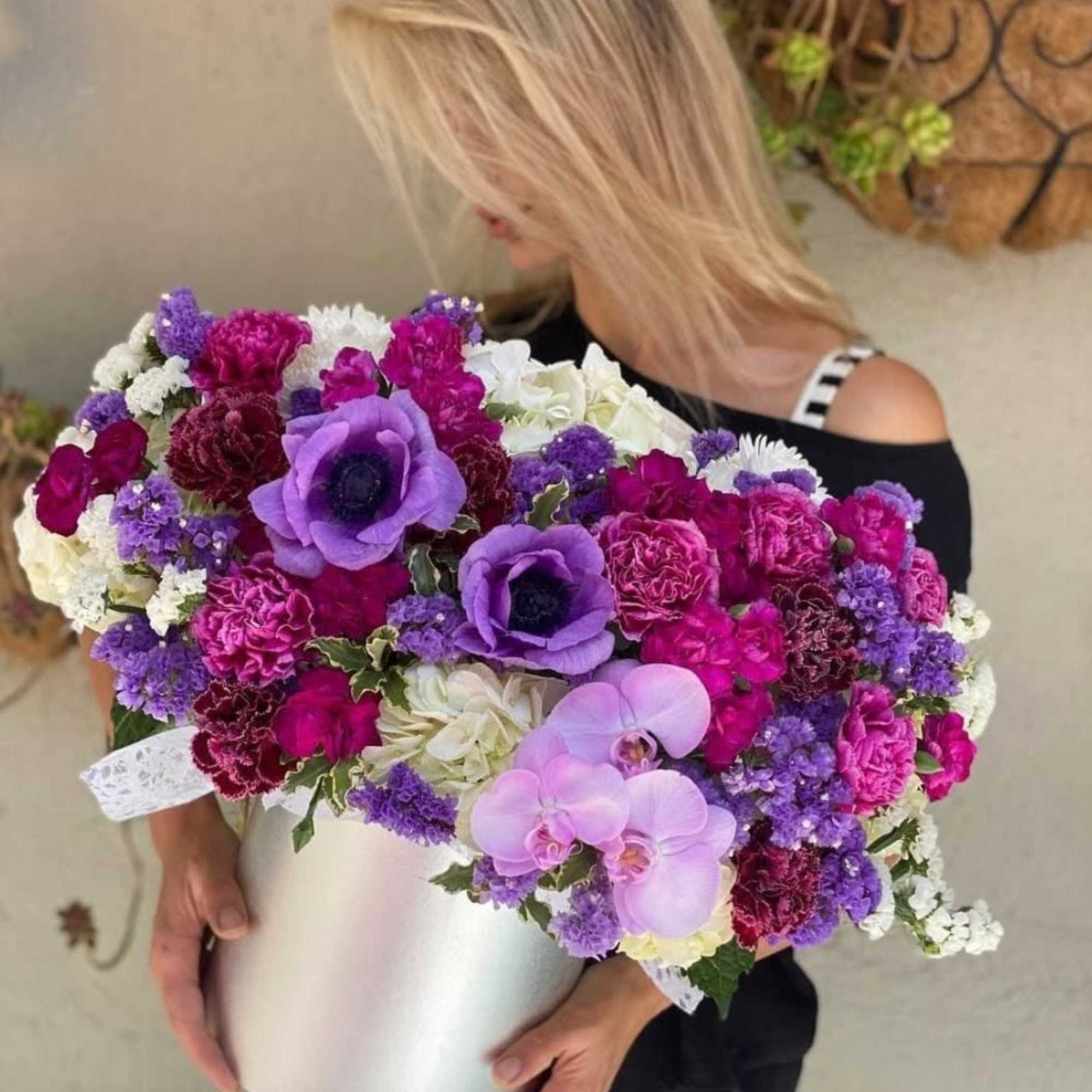 Woman holding a large purple, pink, and white flower arrangement in a white box