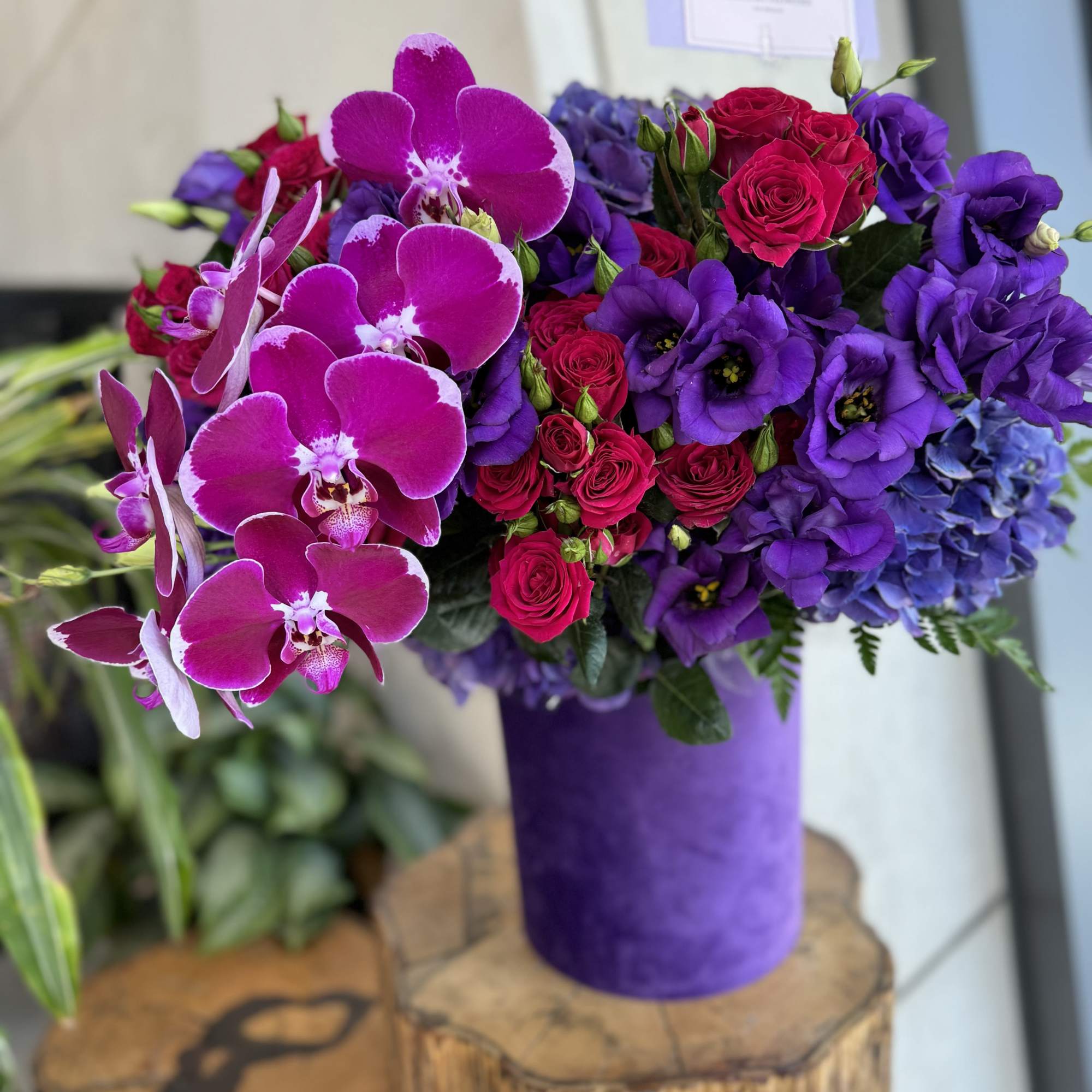 Purple orchids and roses arranged in a purple vase