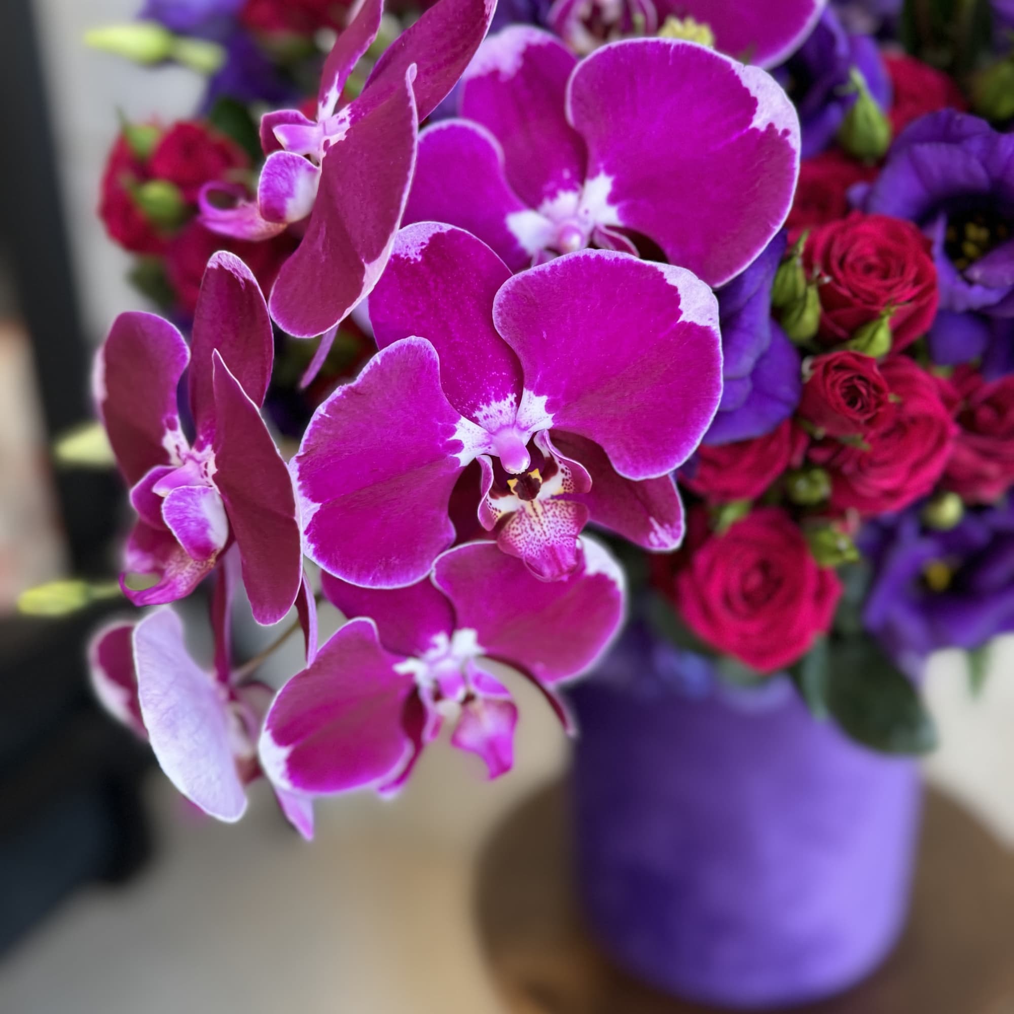 Bouquet of magenta orchids and roses in a purple vase