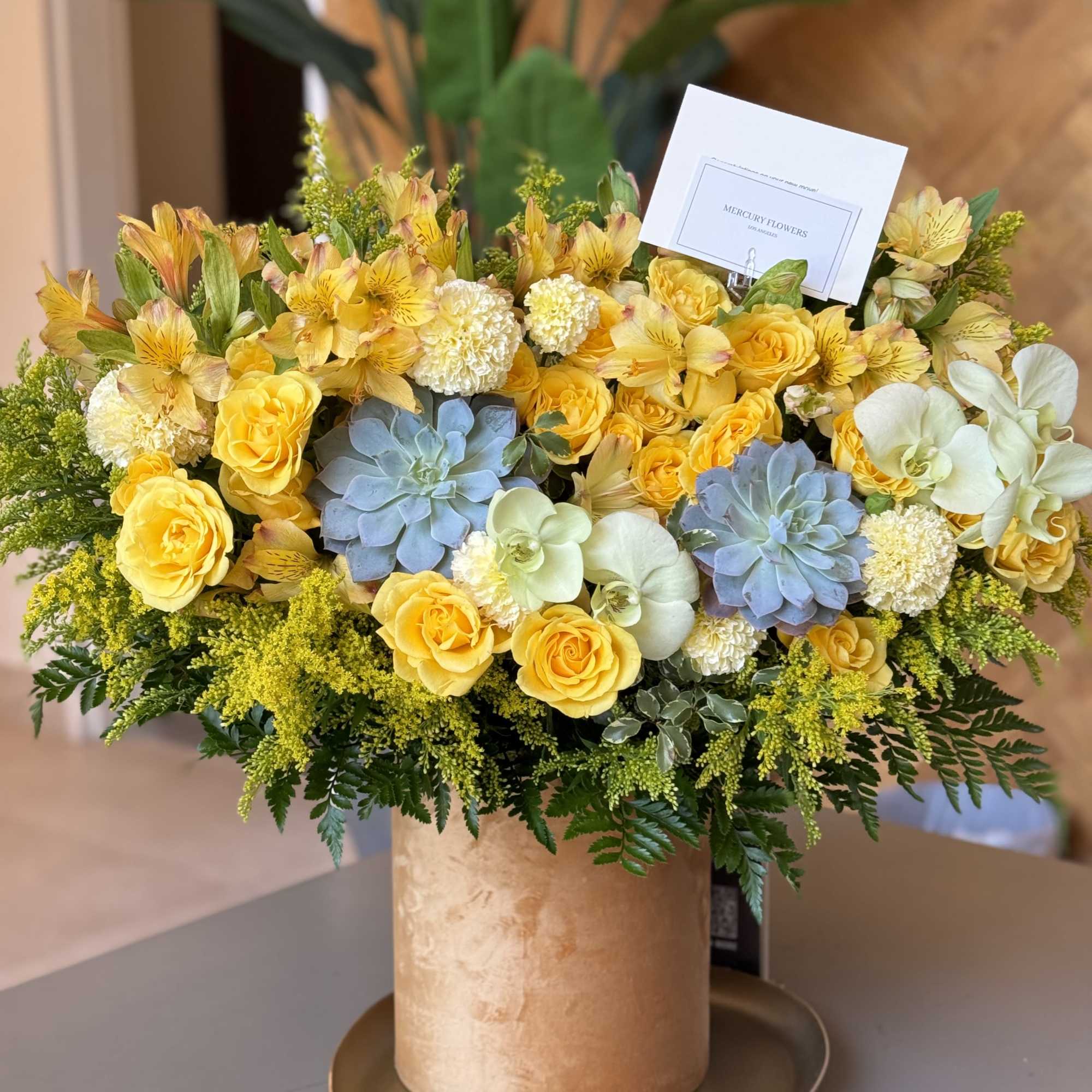 Yellow roses and orchids arranged in a gold hatbox